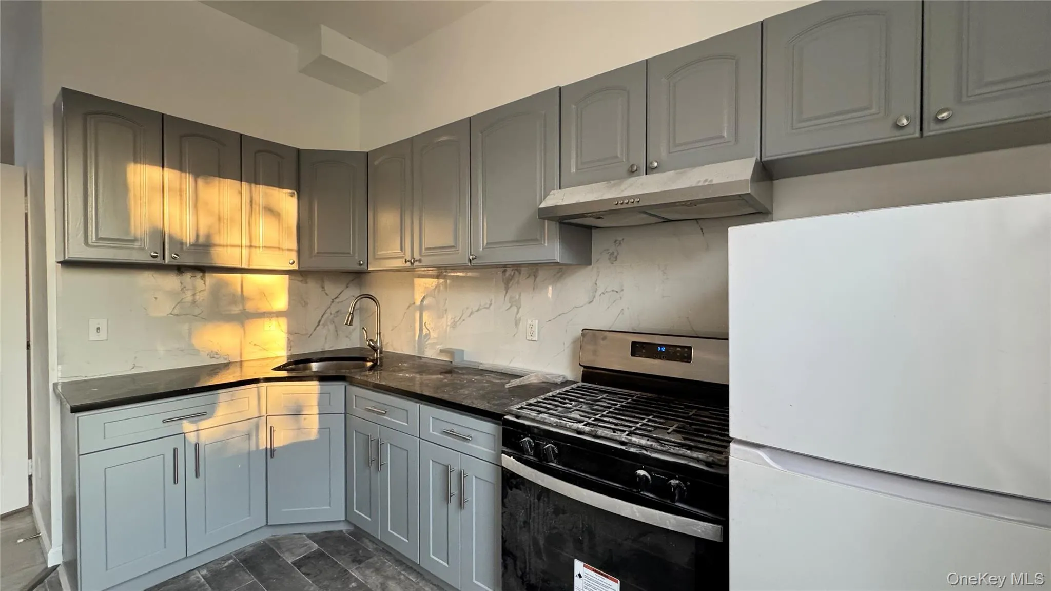 Kitchen with freestanding refrigerator, gas range, under cabinet range hood, tasteful backsplash, and dark stone counters Kitchen with freestanding refrigerator, gas range, under cabinet range hood, tasteful backsplash, and dark stone counters