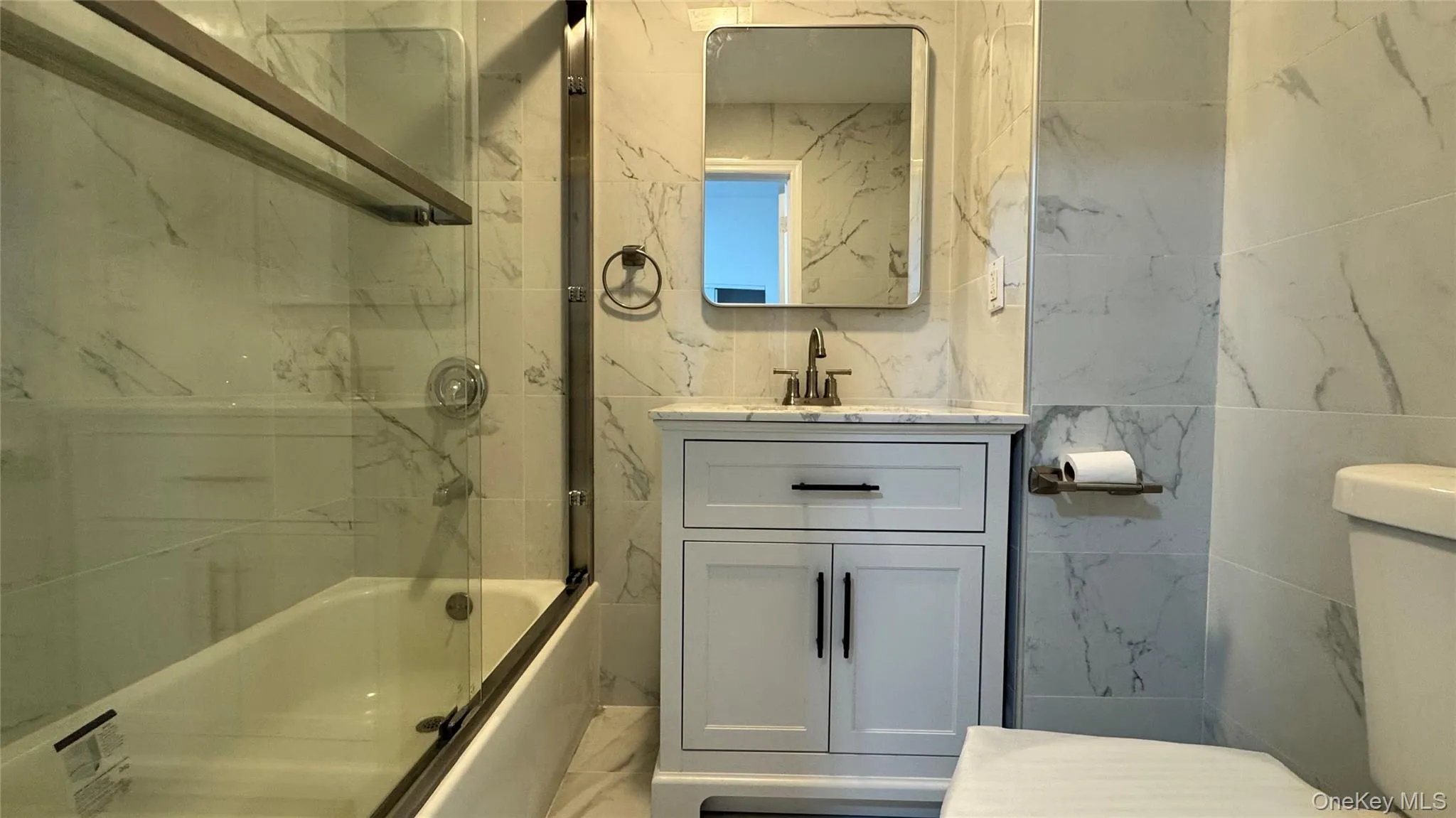 Full bathroom with vanity, shower / bath combination with glass door, and tile walls Full bathroom with vanity, shower / bath combination with glass door, and tile walls