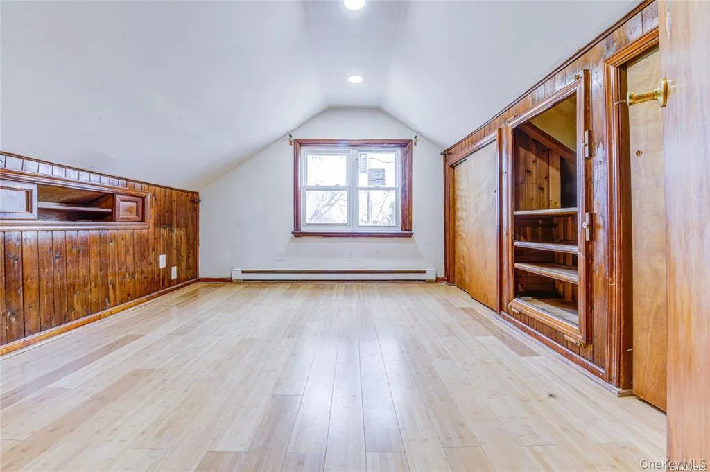 Bonus room featuring wooden walls, vaulted ceiling, light wood-style floors, a baseboard heating unit, and built in shelves Bonus room featuring wooden walls, vaulted ceiling, light wood-style floors, a baseboard heating unit, and built in shelves
