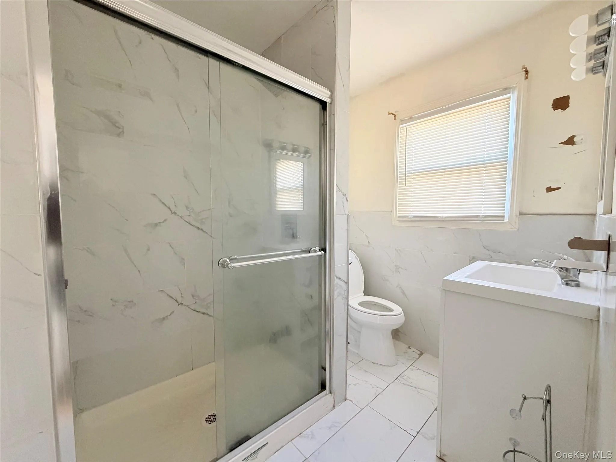 Full bath featuring tile walls, vanity, a wainscoted wall, light marble finish floors, and a marble finish shower Full bath featuring tile walls, vanity, a wainscoted wall, light marble finish floors, and a marble finish shower