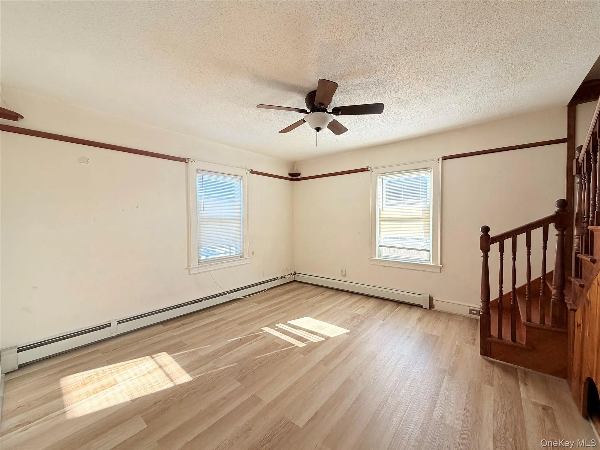 Unfurnished room featuring light wood finished floors, a textured ceiling, plenty of natural light, ceiling fan, and baseboard heating Unfurnished room featuring light wood finished floors, a textured ceiling, plenty of natural light, ceiling fan, and baseboard heating