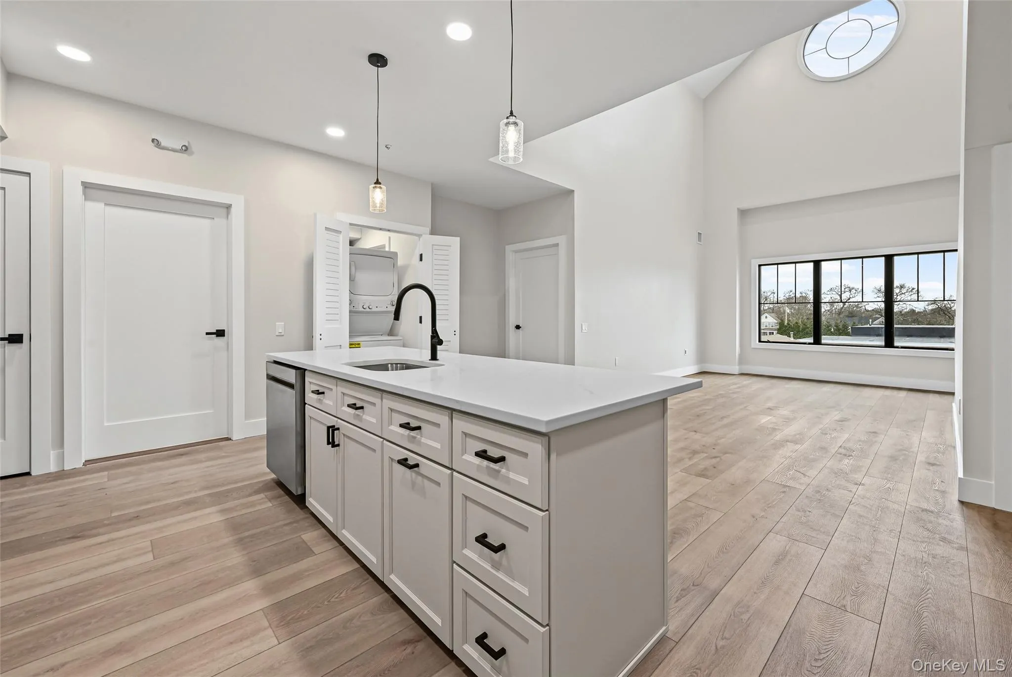 Kitchen featuring white cabinets, hanging light fixtures, light wood-style flooring, a center island with sink, and vaulted ceiling Kitchen featuring white cabinets, hanging light fixtures, light wood-style flooring, a center island with sink, and vaulted ceiling