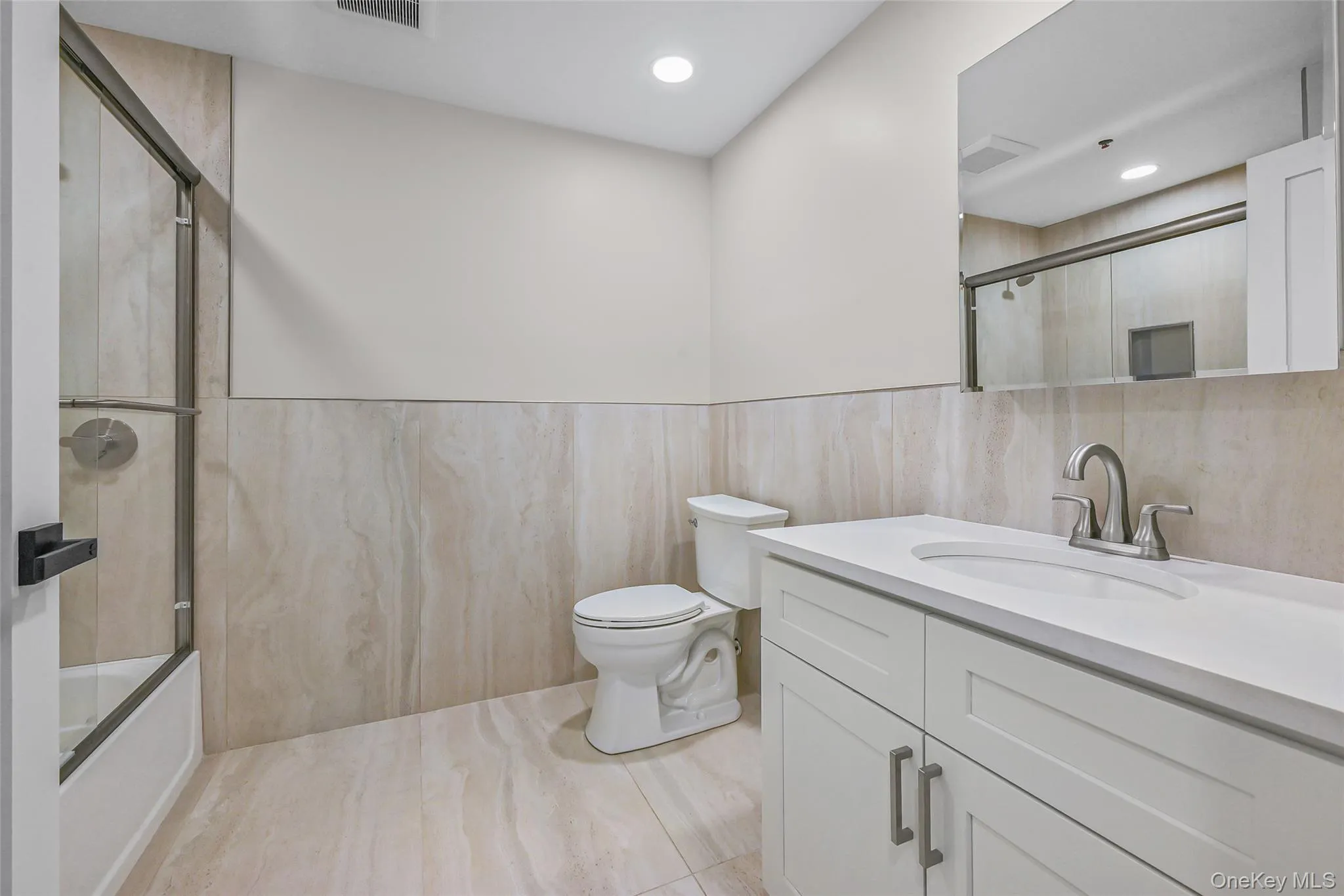 Bathroom with vanity, tile walls, combined bath / shower with glass door, a wainscoted wall, and recessed lighting Bathroom with vanity, tile walls, combined bath / shower with glass door, a wainscoted wall, and recessed lighting