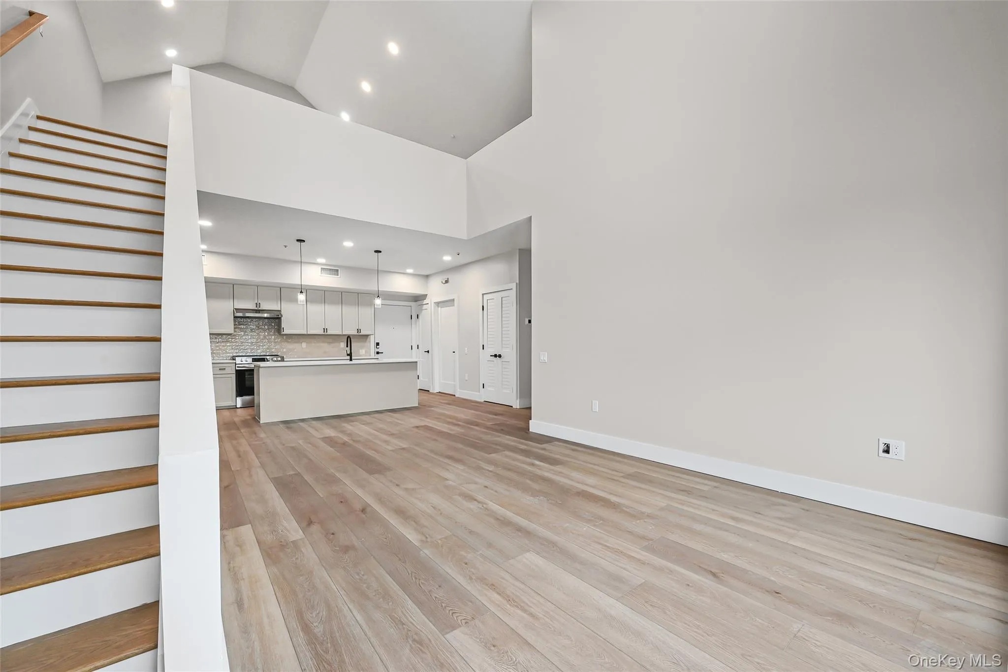 Unfurnished living room featuring light wood-type flooring, recessed lighting, high vaulted ceiling, and stairway Unfurnished living room featuring light wood-type flooring, recessed lighting, high vaulted ceiling, and stairway