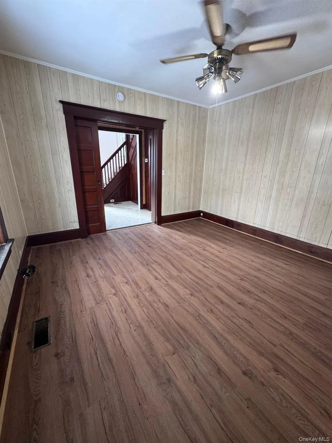 Empty room featuring dark wood-style flooring, wood walls, crown molding, and ceiling fan Empty room featuring dark wood-style flooring, wood walls, crown molding, and ceiling fan