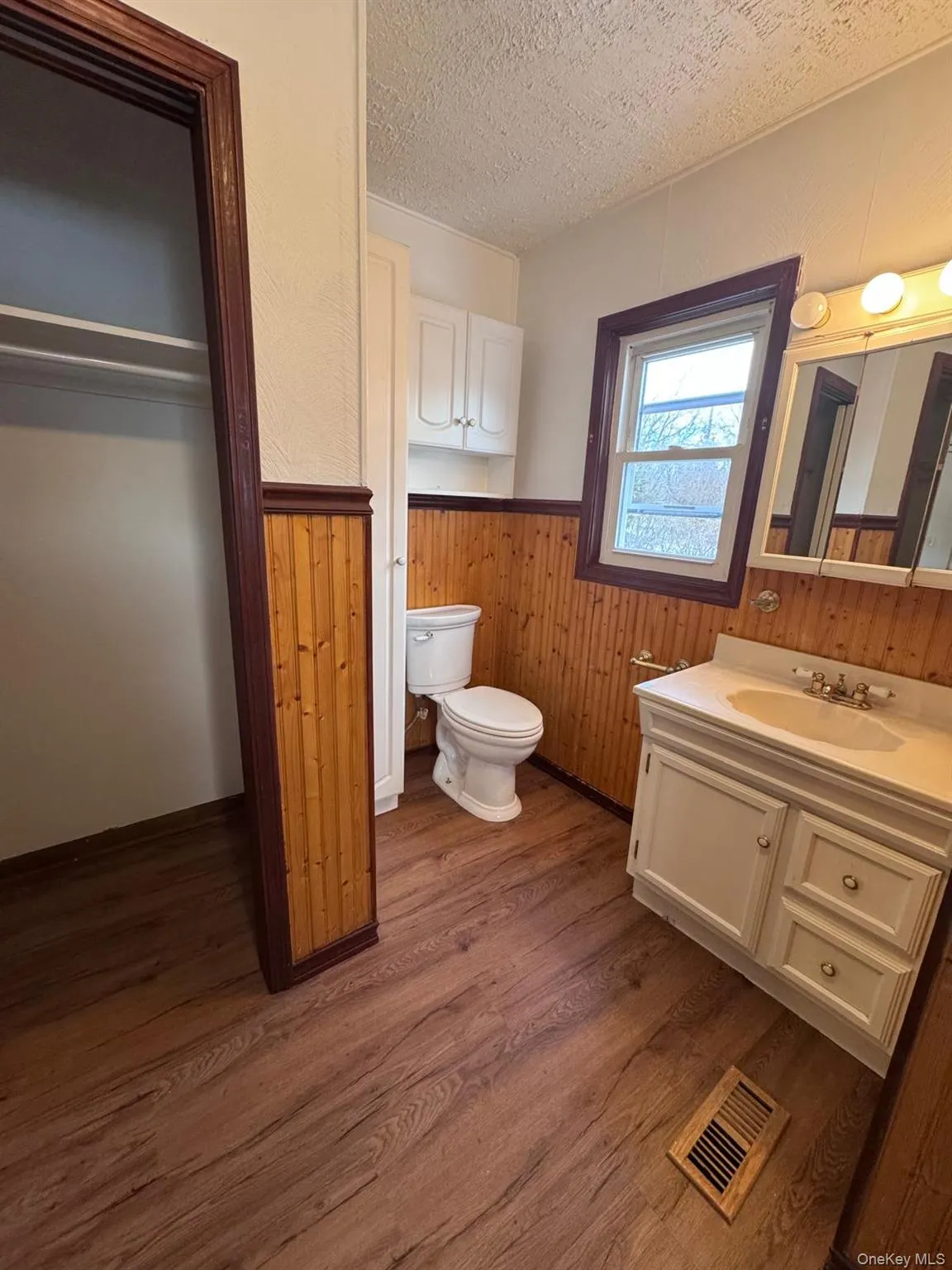 Half bathroom with vanity, a wainscoted wall, wood walls, a textured ceiling, and dark wood-type flooring Half bathroom with vanity, a wainscoted wall, wood walls, a textured ceiling, and dark wood-type flooring