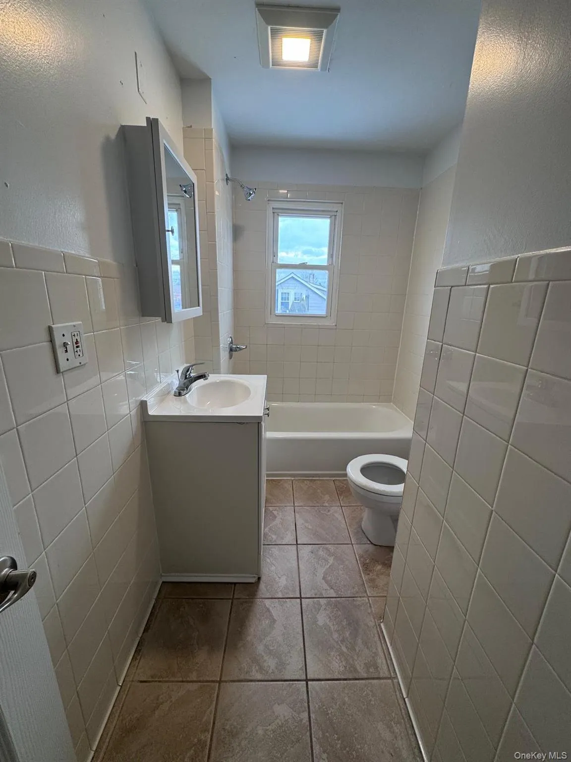 Full bathroom with tile walls, vanity, tub / shower combination, a wainscoted wall, and a textured wall Full bathroom with tile walls, vanity, tub / shower combination, a wainscoted wall, and a textured wall