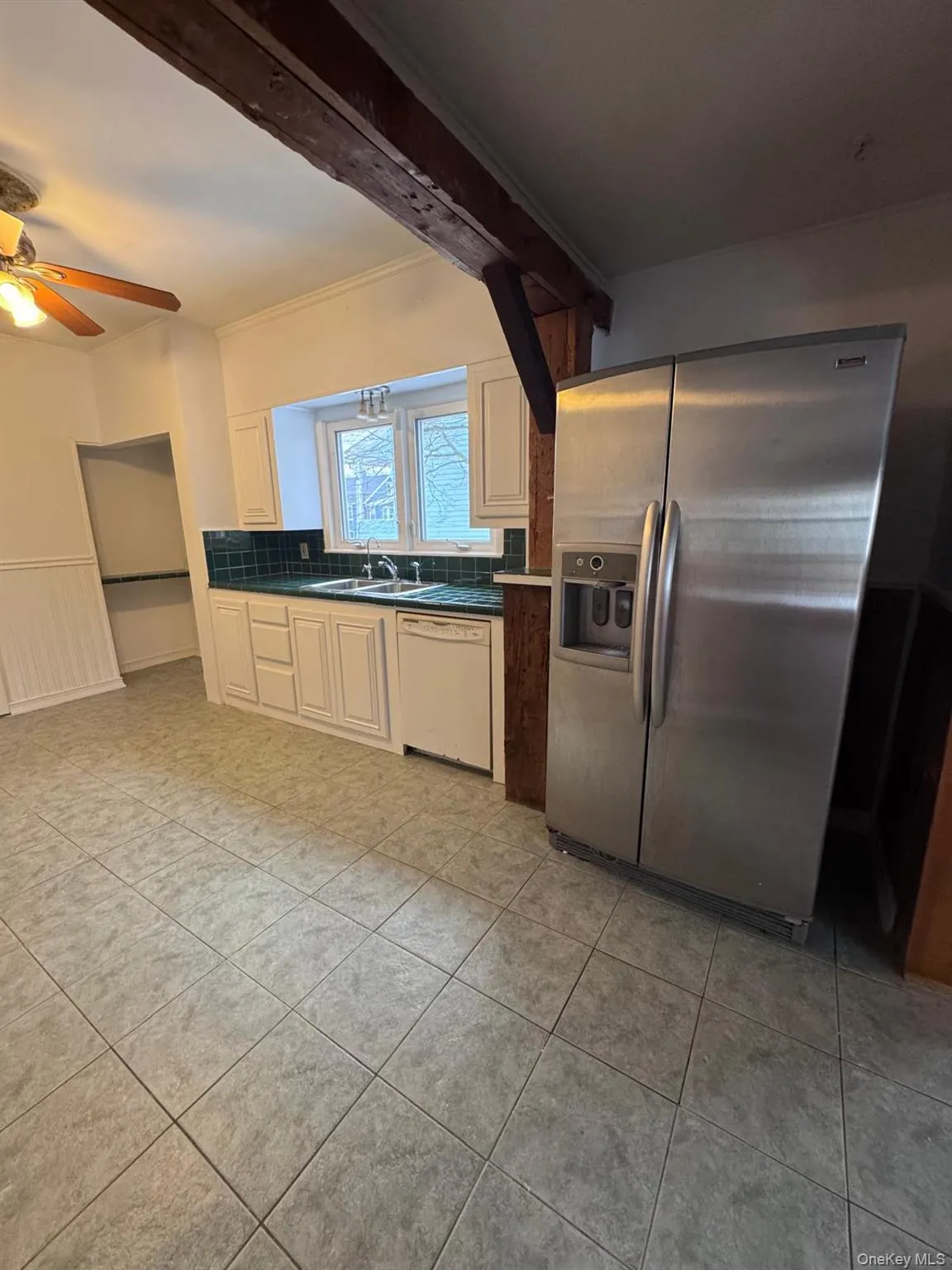 Kitchen featuring stainless steel fridge with ice dispenser, dark countertops, dishwasher, light tile patterned floors, and a ceiling fan Kitchen featuring stainless steel fridge with ice dispenser, dark countertops, dishwasher, light tile patterned floors, and a ceiling fan
