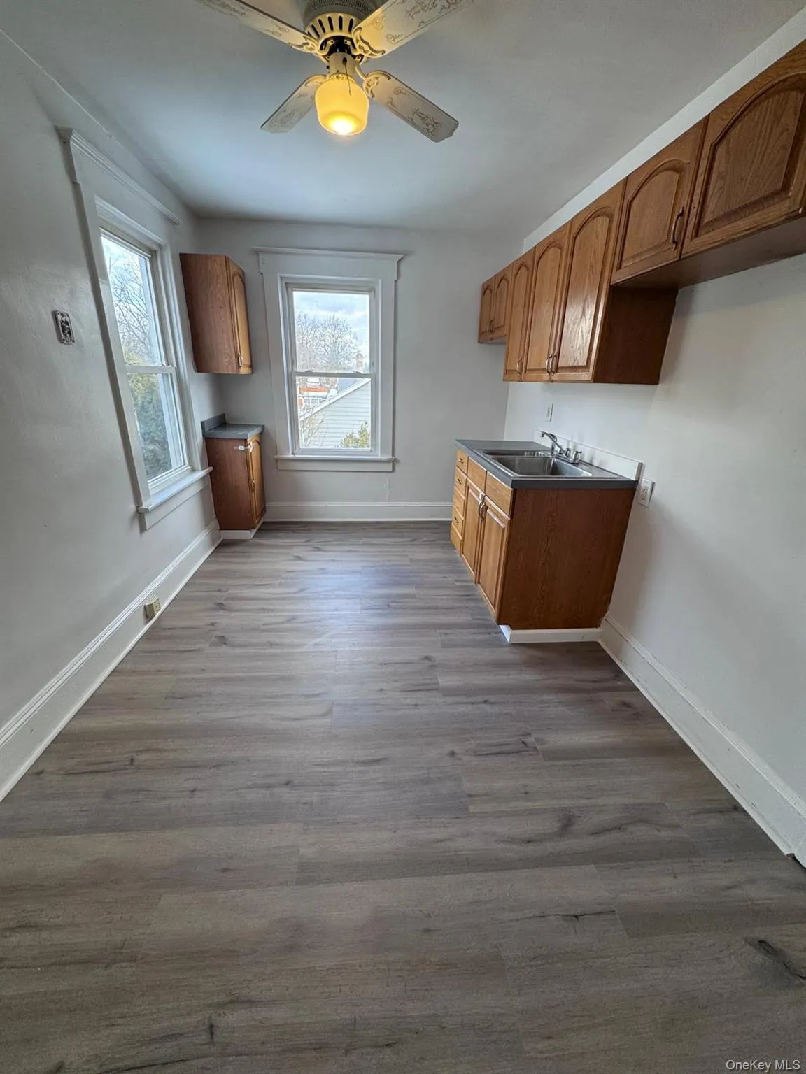 Kitchen with brown cabinetry, dark countertops, dark wood-style flooring, and a ceiling fan Kitchen with brown cabinetry, dark countertops, dark wood-style flooring, and a ceiling fan