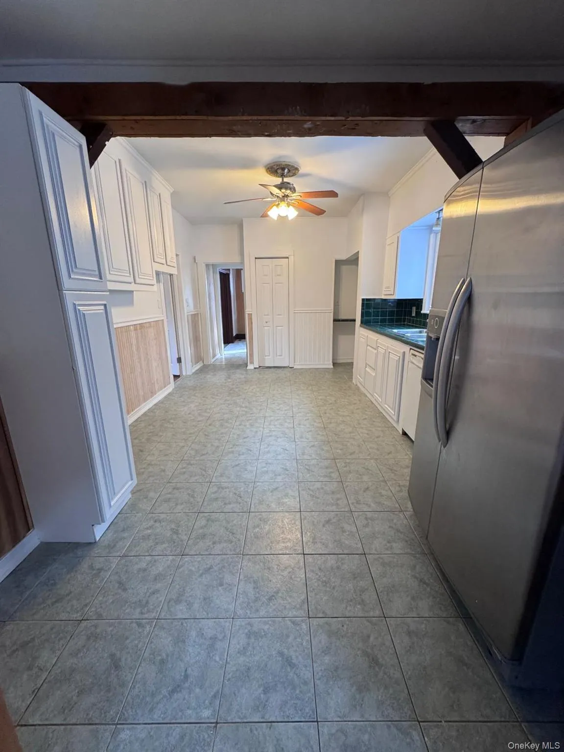 Kitchen with stainless steel fridge, white cabinets, ceiling fan, wainscoting, and light tile patterned flooring Kitchen with stainless steel fridge, white cabinets, ceiling fan, wainscoting, and light tile patterned flooring