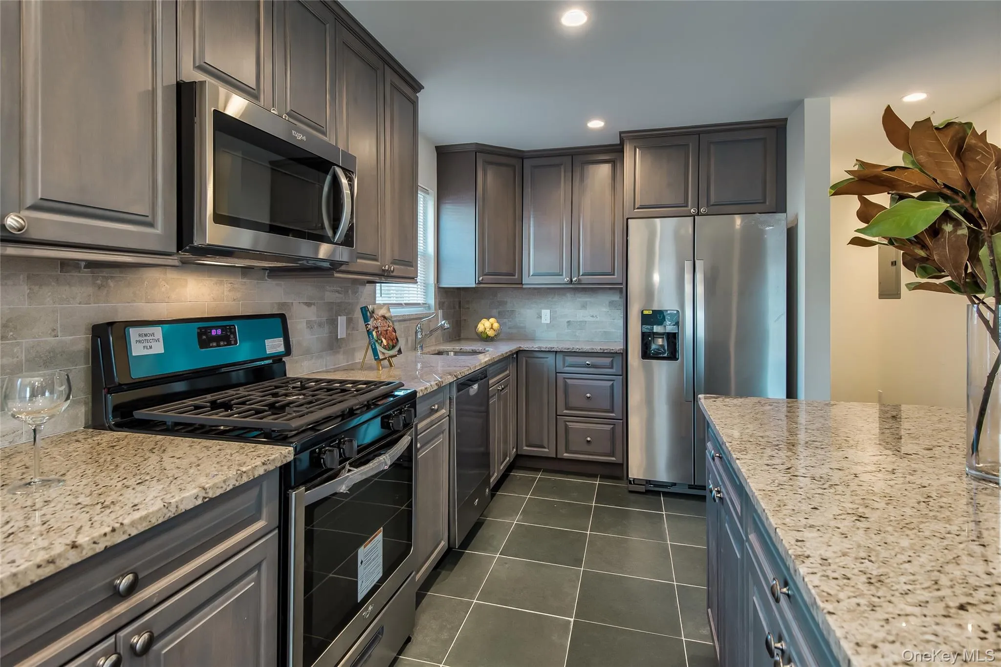 Kitchen with stainless steel appliances, light stone counters, dark tile patterned flooring, recessed lighting, and backsplash Kitchen with stainless steel appliances, light stone counters, dark tile patterned flooring, recessed lighting, and backsplash