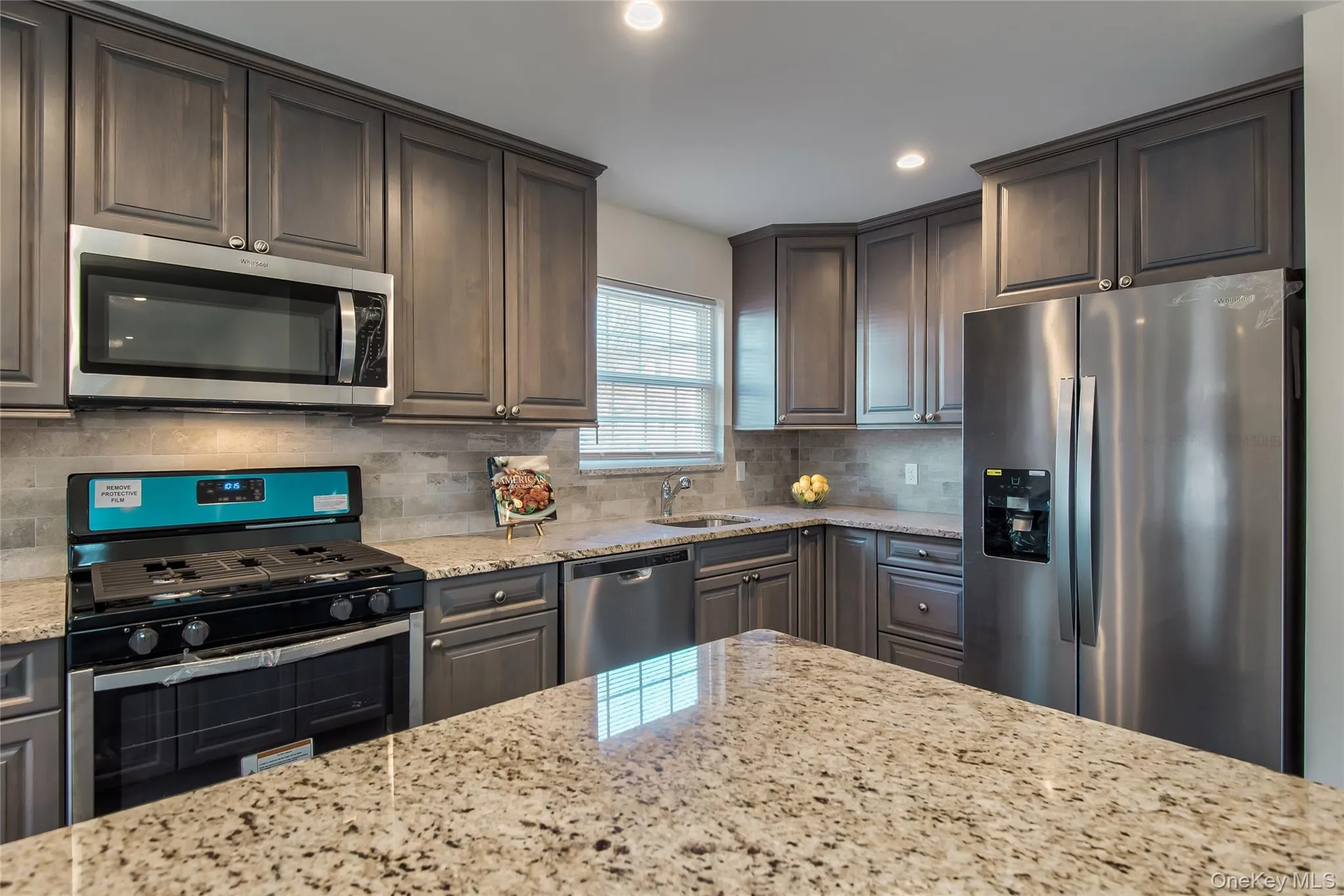 Kitchen with stainless steel appliances, light stone countertops, recessed lighting, backsplash, and dark brown cabinetry Kitchen with stainless steel appliances, light stone countertops, recessed lighting, backsplash, and dark brown cabinetry