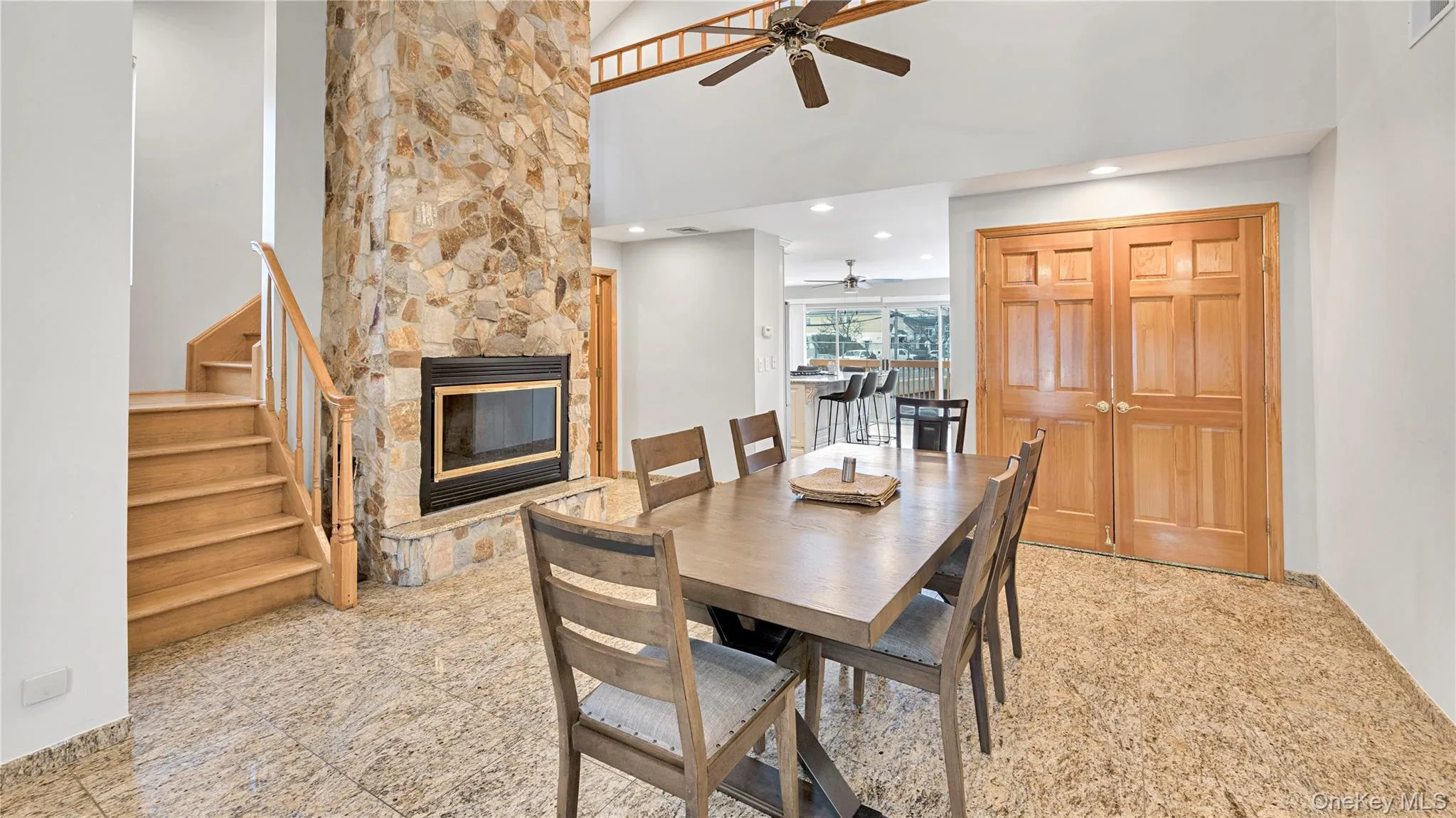 Dining area featuring granite tiled floors, a stone fireplace, a high ceiling, a ceiling fan, and recessed lighting Dining area featuring granite tiled floors, a stone fireplace, a high ceiling, a ceiling fan, and recessed lighting