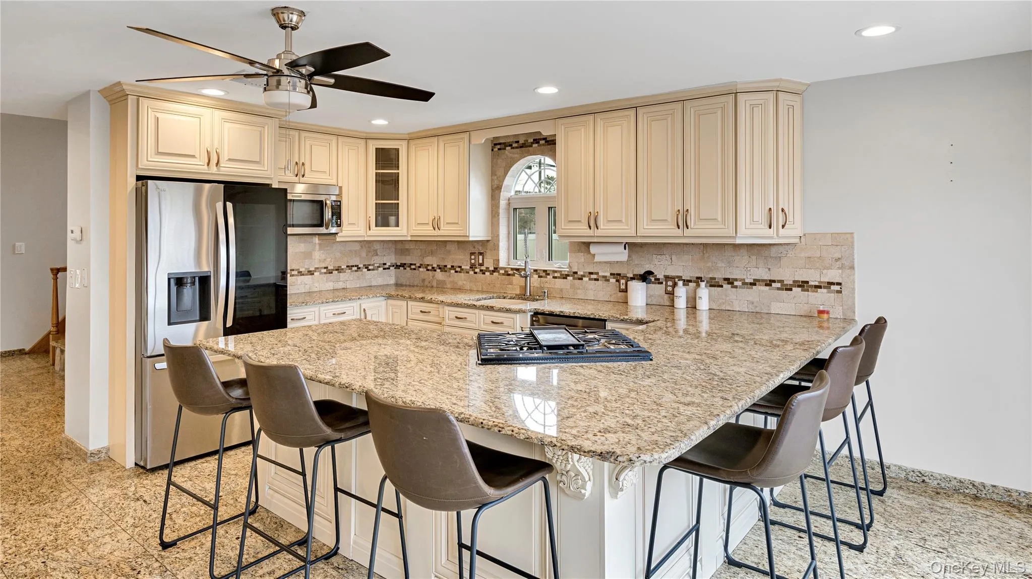 Kitchen with cream cabinetry, a peninsula, a breakfast bar, appliances with stainless steel finishes, and light stone countertops Kitchen with cream cabinetry, a peninsula, a breakfast bar, appliances with stainless steel finishes, and light stone countertops