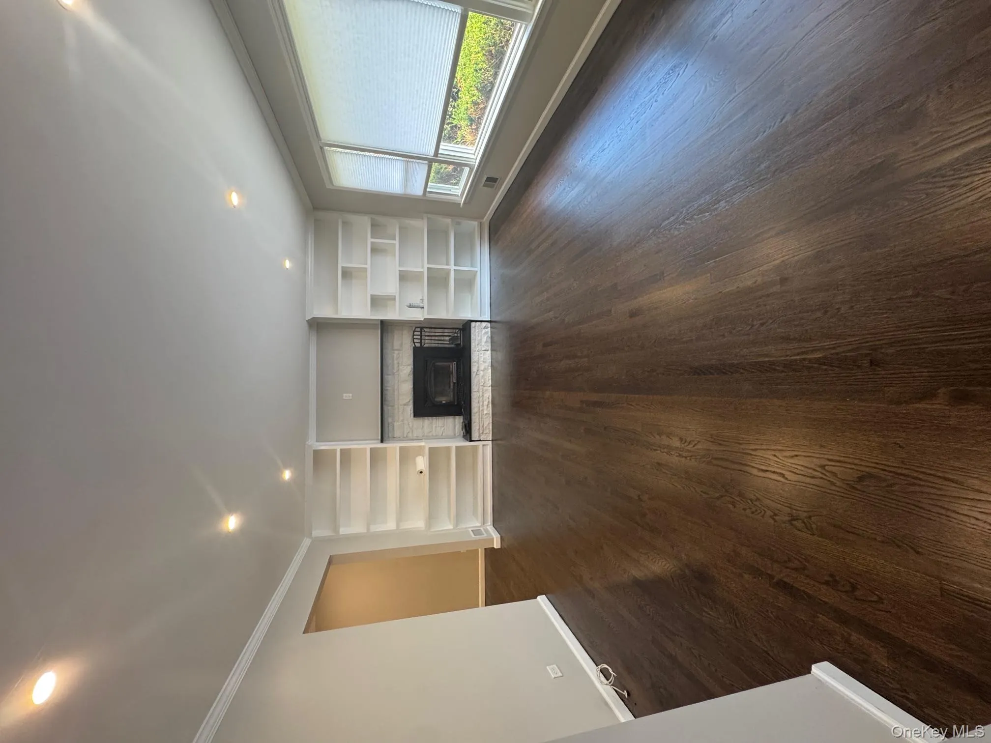 Unfurnished living room with crown molding, recessed lighting, built in features, a fireplace with raised hearth, and dark wood-type flooring Unfurnished living room with crown molding, recessed lighting, built in features, a fireplace with raised hearth, and dark wood-type flooring
