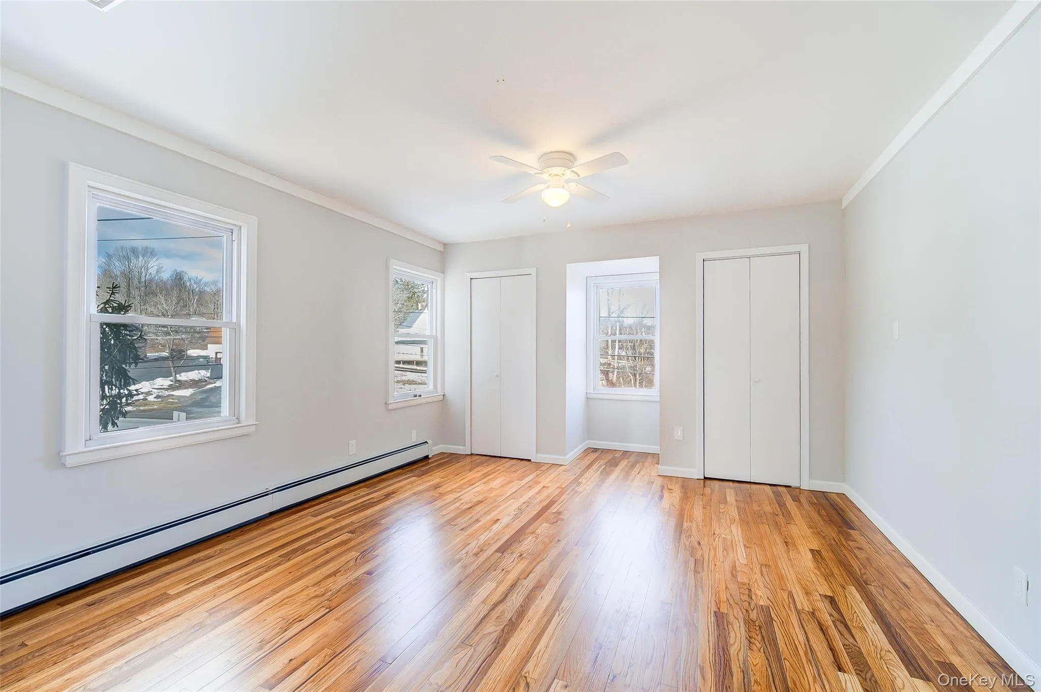 Second bedroom featuring multiple closets, light wood finished floors, a baseboard heating unit, crown molding, and a ceiling fan Second bedroom featuring multiple closets, light wood finished floors, a baseboard heating unit, crown molding, and a ceiling fan