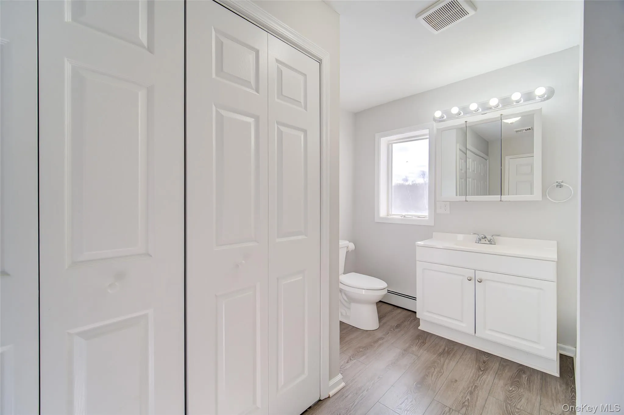 Bathroom featuring a closet, vanity, light wood-type flooring, and a baseboard radiator Bathroom featuring a closet, vanity, light wood-type flooring, and a baseboard radiator