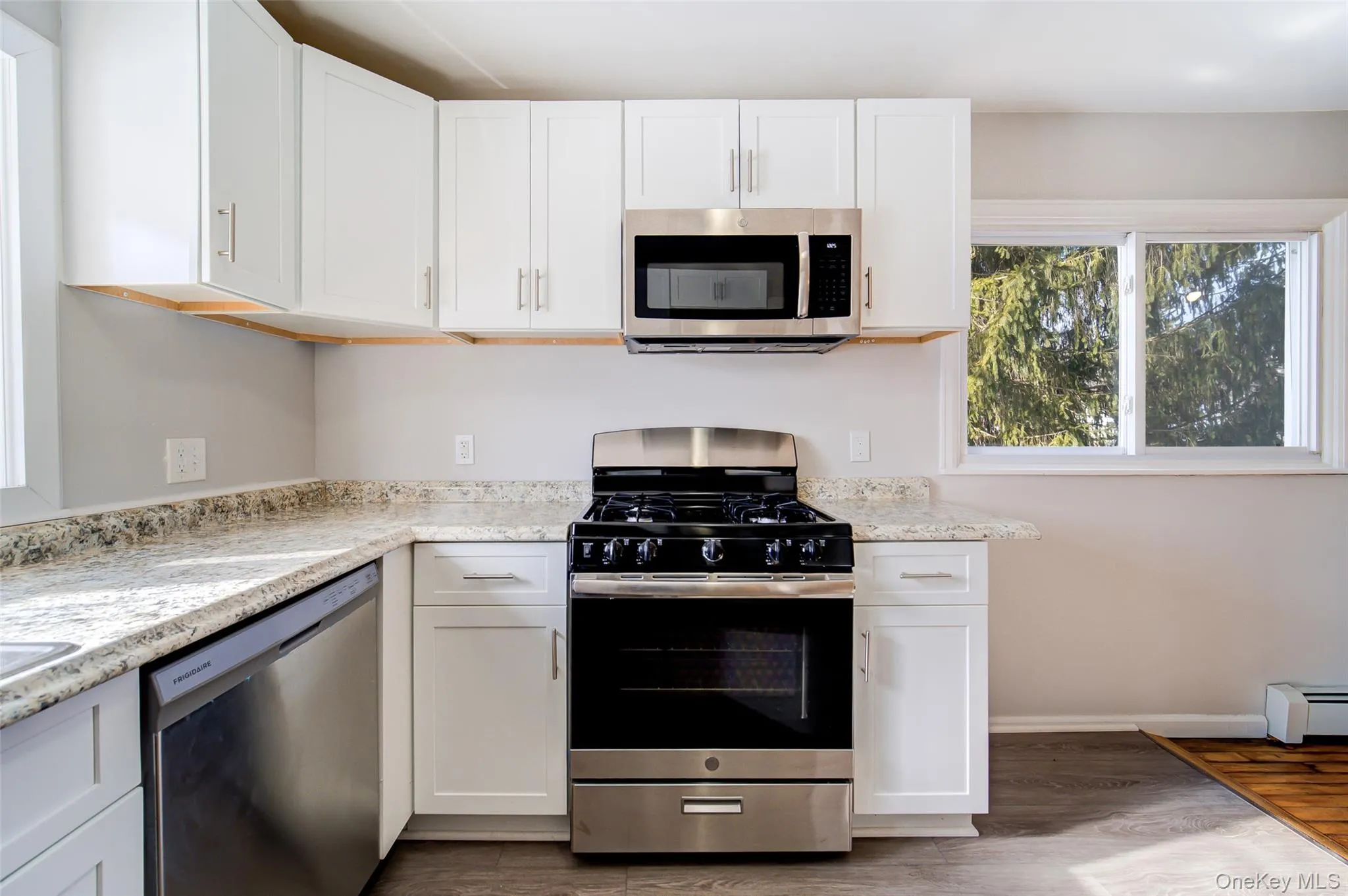 Kitchen featuring stainless steel appliances, white cabinets, light wood-type flooring, and a baseboard radiator Kitchen featuring stainless steel appliances, white cabinets, light wood-type flooring, and a baseboard radiator