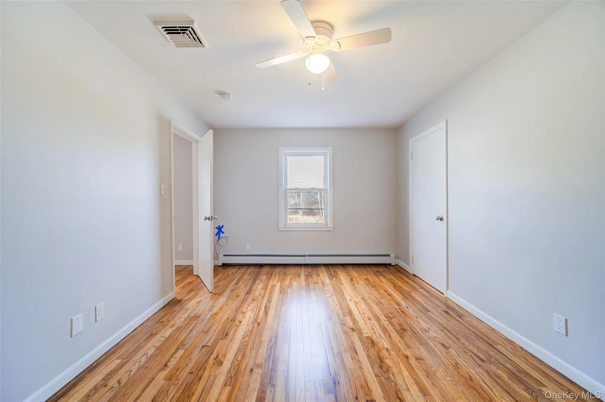 First bedroom with hardwood flooring, a baseboard radiator, and a ceiling fan First bedroom with hardwood flooring, a baseboard radiator, and a ceiling fan