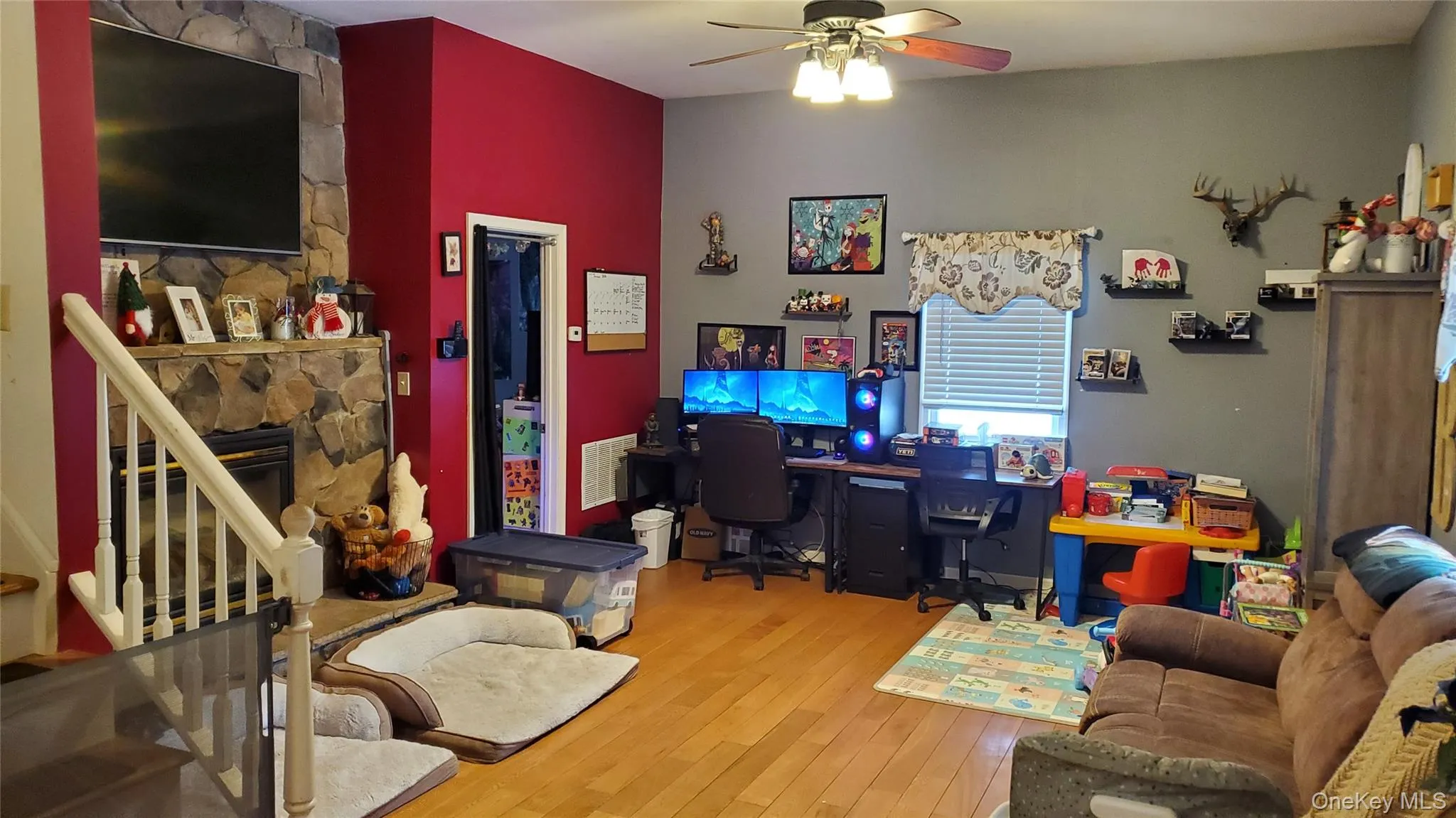 Home office featuring wood-type flooring, ceiling fan, and a stone fireplace Home office featuring wood-type flooring, ceiling fan, and a stone fireplace