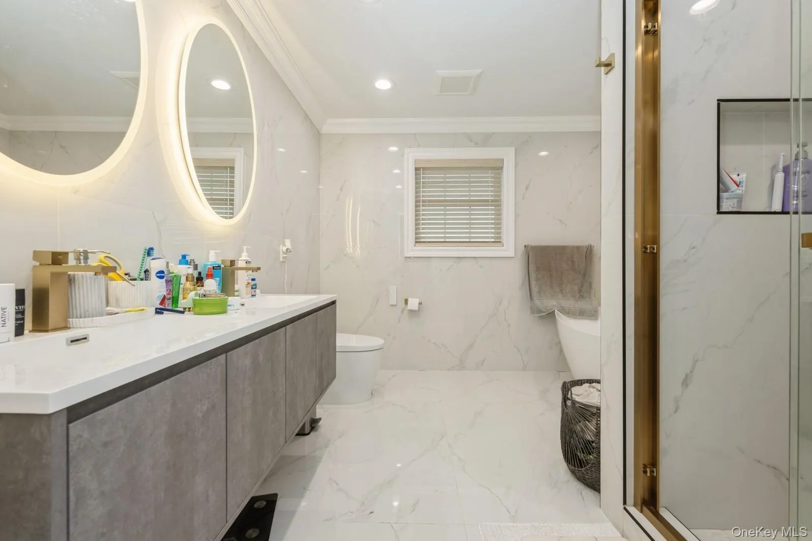 Bathroom featuring stone wall, double vanity, crown molding, light marble finish flooring, and recessed lighting Bathroom featuring stone wall, double vanity, crown molding, light marble finish flooring, and recessed lighting