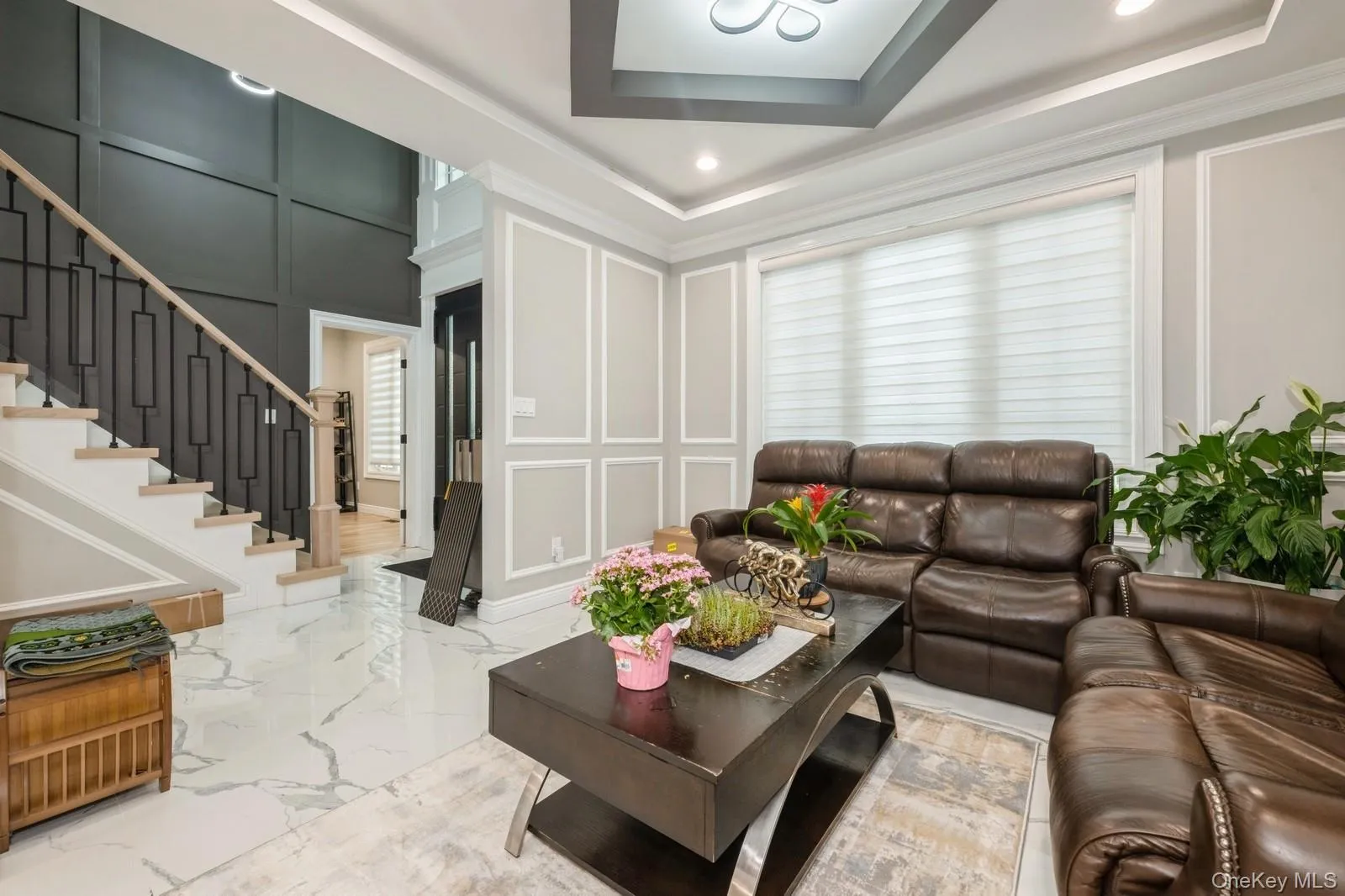 Living room with a decorative wall, stairs, marble tiled flooring, ornamental molding, and recessed lighting Living room with a decorative wall, stairs, marble tiled flooring, ornamental molding, and recessed lighting