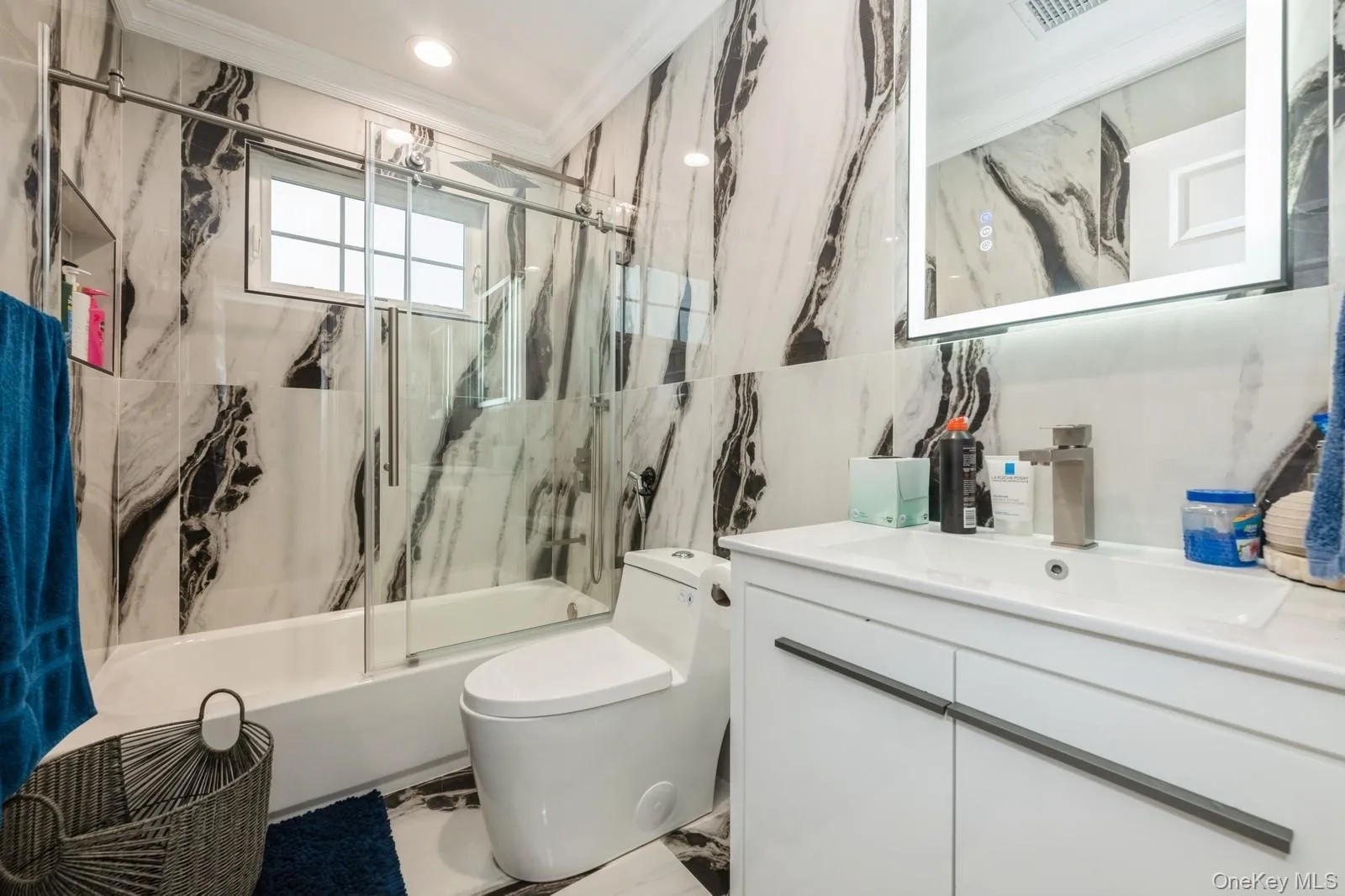 Full bath with marble tiled flooring, shower / bath combination with glass door, tile walls, vanity, and ornamental molding Full bath with marble tiled flooring, shower / bath combination with glass door, tile walls, vanity, and ornamental molding