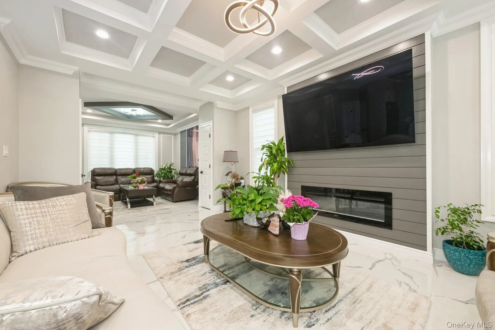 Living area with marble tiled floors, coffered ceiling, ornamental molding, a large fireplace, and recessed lighting Living area with marble tiled floors, coffered ceiling, ornamental molding, a large fireplace, and recessed lighting