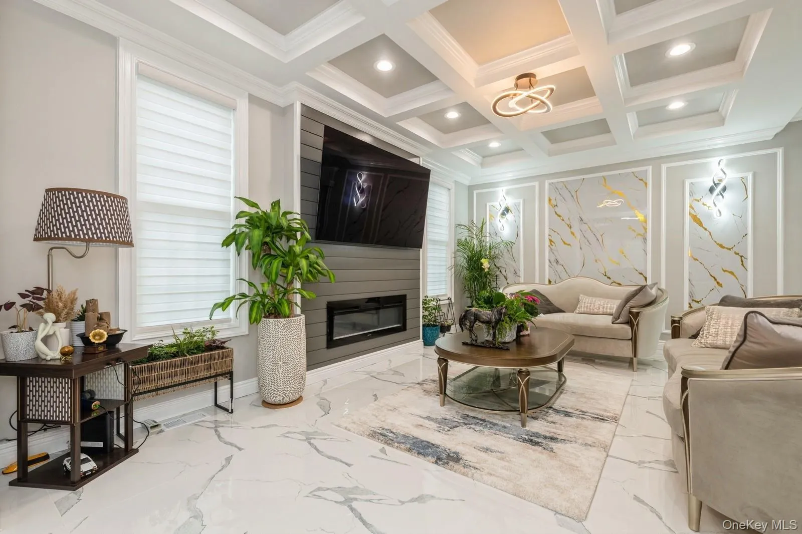 Living area featuring marble tiled floors, a glass covered fireplace, a chandelier, recessed lighting, and coffered ceiling Living area featuring marble tiled floors, a glass covered fireplace, a chandelier, recessed lighting, and coffered ceiling