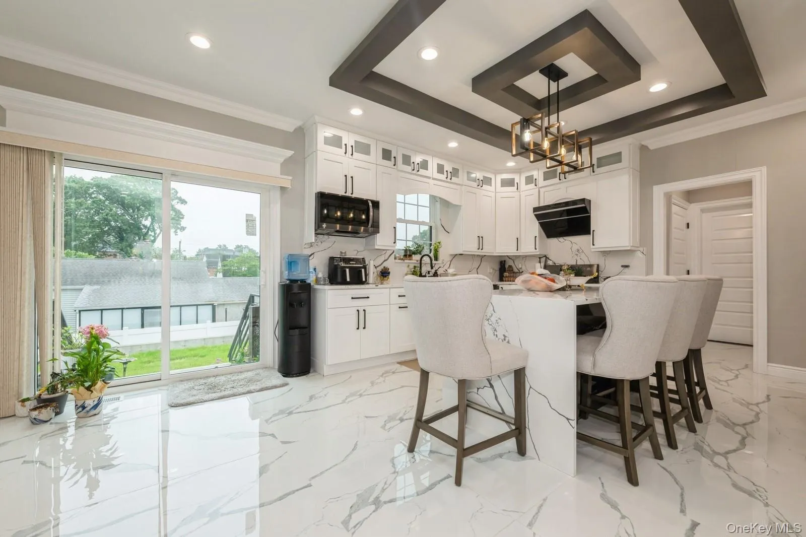 Kitchen with white cabinets, a breakfast bar, decorative light fixtures, light marble finish flooring, and a kitchen island Kitchen with white cabinets, a breakfast bar, decorative light fixtures, light marble finish flooring, and a kitchen island