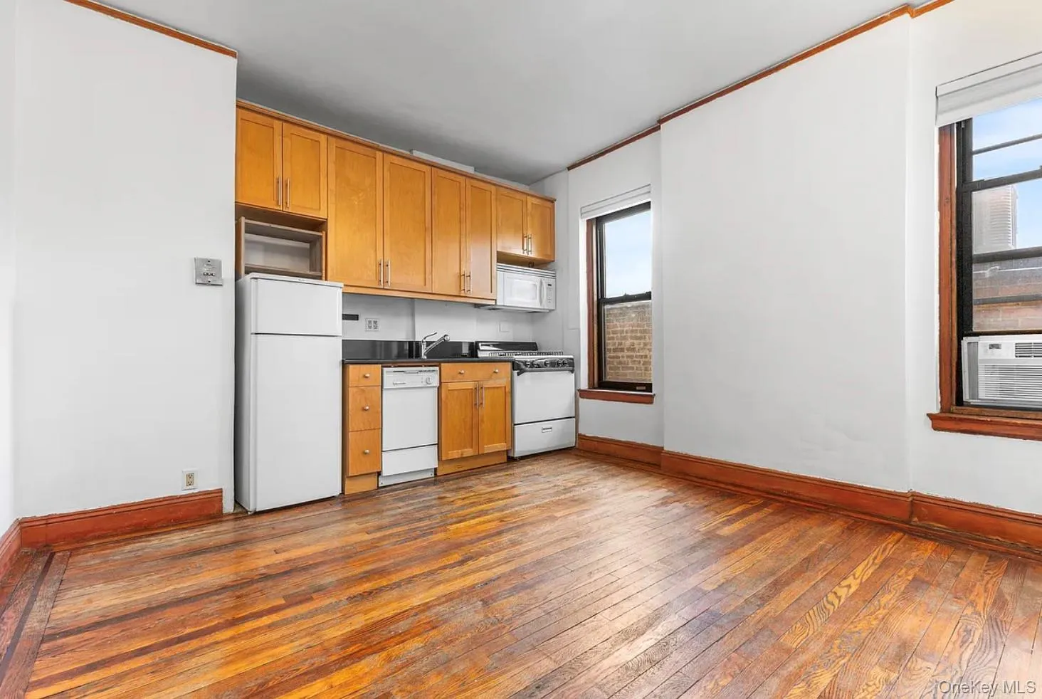 Kitchen featuring white appliances, brown cabinetry, dark wood-style flooring, dark countertops, and ornamental molding Kitchen featuring white appliances, brown cabinetry, dark wood-style flooring, dark countertops, and ornamental molding