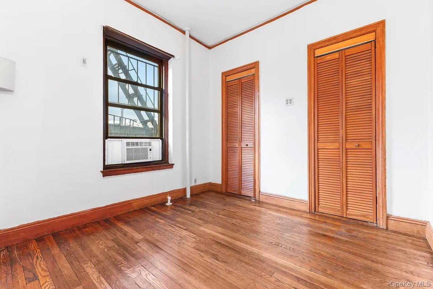 Unfurnished bedroom featuring two closets, wood-type flooring, ornamental molding, and cooling unit Unfurnished bedroom featuring two closets, wood-type flooring, ornamental molding, and cooling unit