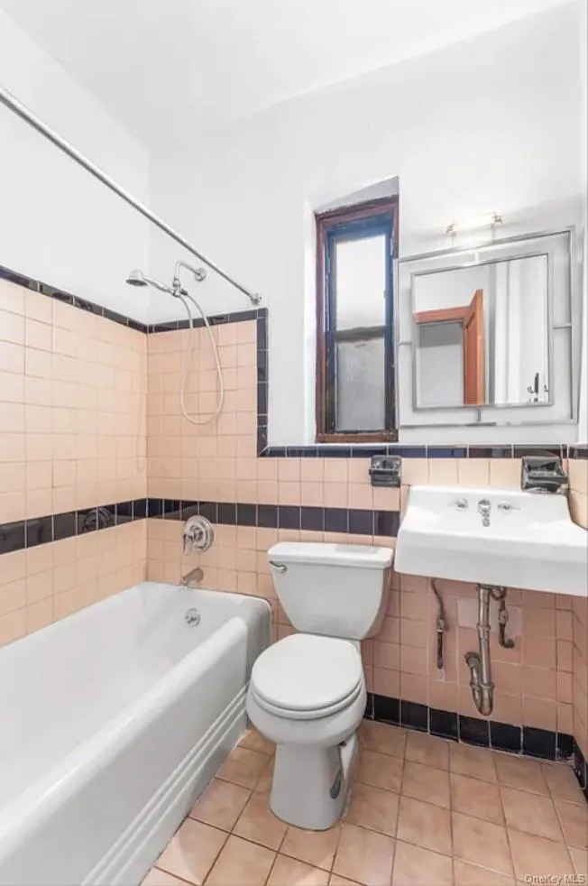 Full bathroom featuring bathing tub / shower combination, tile walls, light tile patterned floors, and wainscoting Full bathroom featuring bathing tub / shower combination, tile walls, light tile patterned floors, and wainscoting