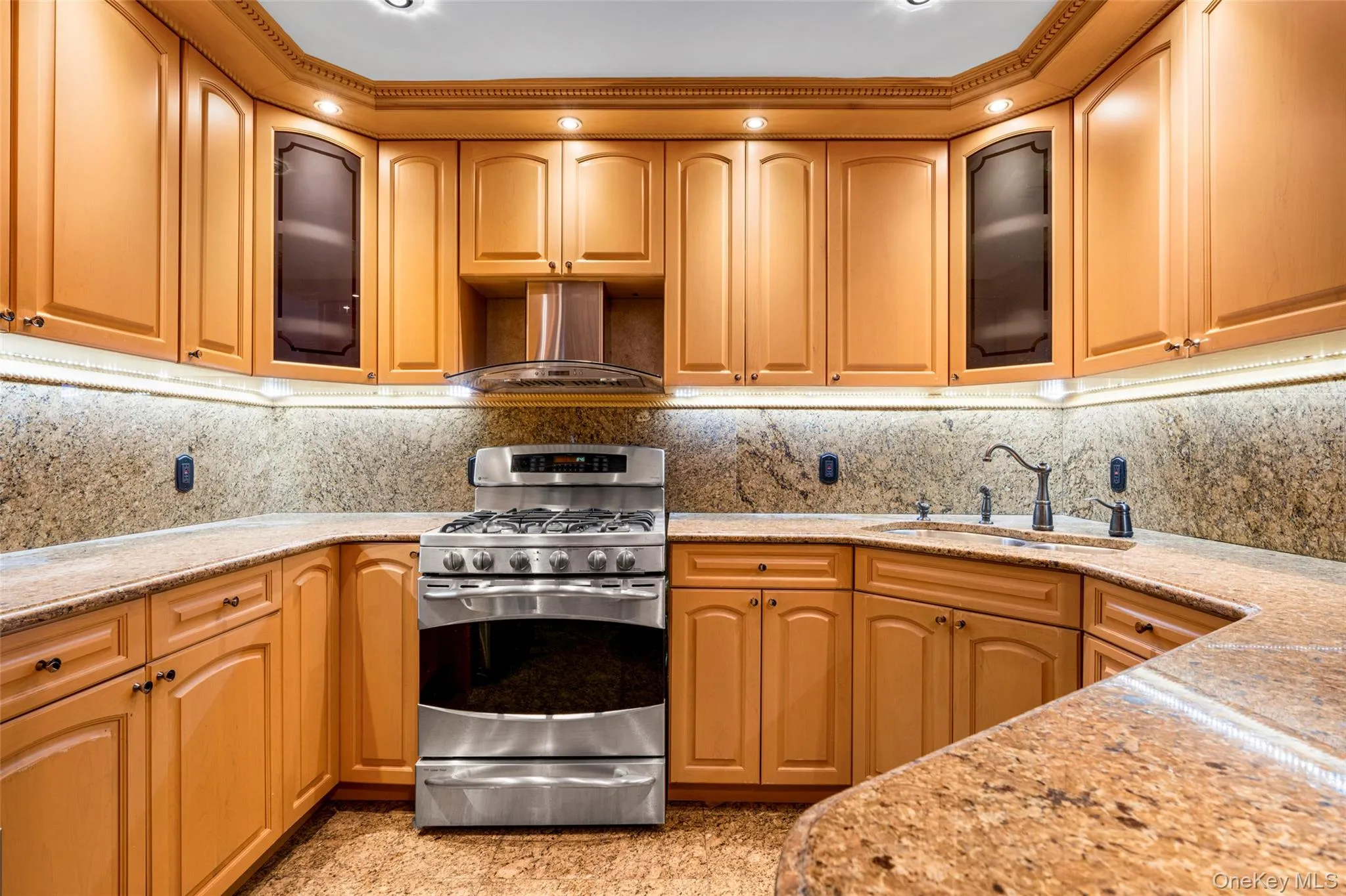 Kitchen featuring glass insert cabinets, gas range, light stone countertops, and ventilation hood Kitchen featuring glass insert cabinets, gas range, light stone countertops, and ventilation hood