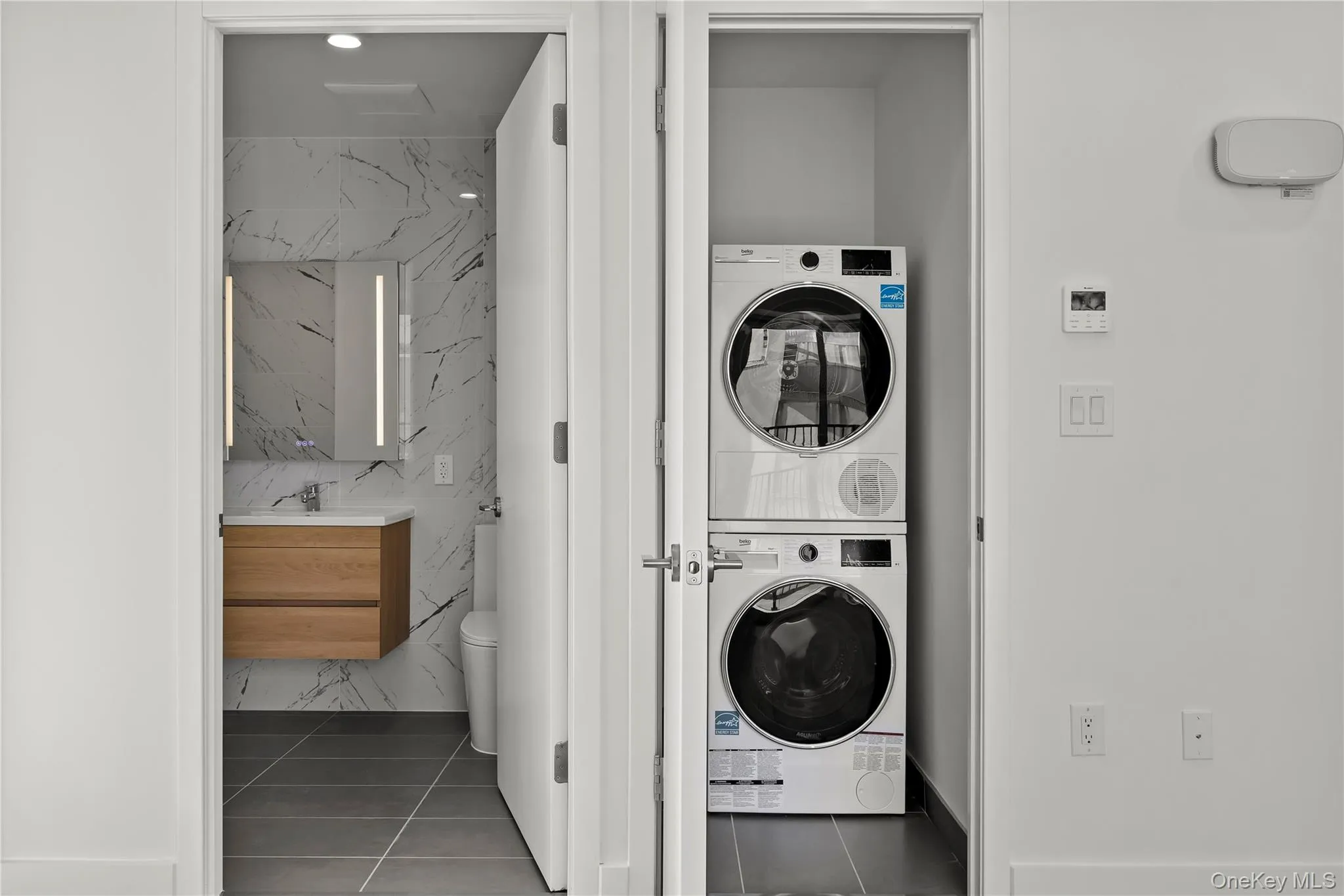 Laundry room with stacked washing machine and dryer, tile walls, and tile patterned flooring Laundry room with stacked washing machine and dryer, tile walls, and tile patterned flooring