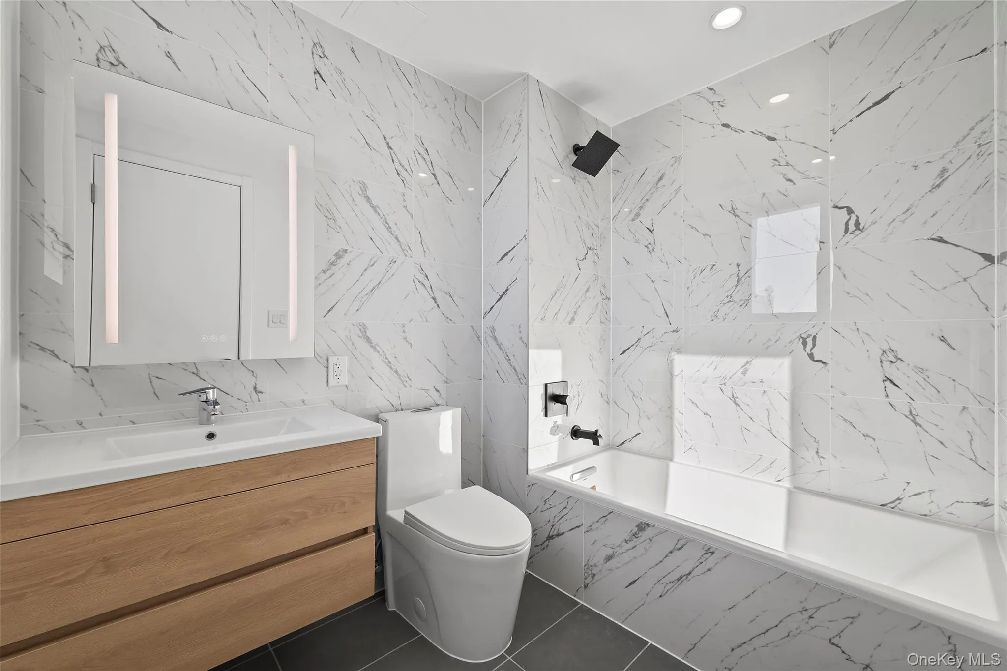 Bathroom featuring tile walls, vanity, a combined bath / shower with marble appearance, recessed lighting, and dark tile patterned flooring Bathroom featuring tile walls, vanity, a combined bath / shower with marble appearance, recessed lighting, and dark tile patterned flooring