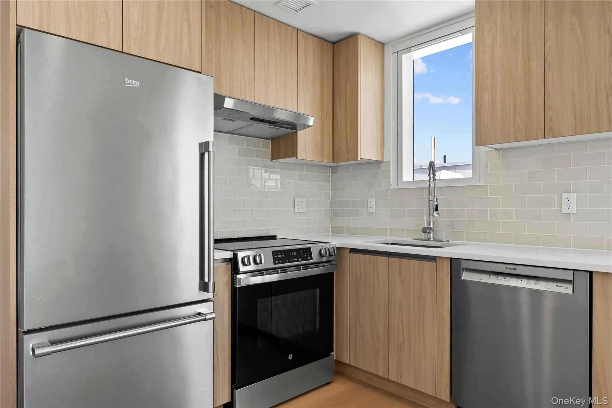 Kitchen featuring appliances with stainless steel finishes, modern cabinets, light stone countertops, and under cabinet range hood Kitchen featuring appliances with stainless steel finishes, modern cabinets, light stone countertops, and under cabinet range hood