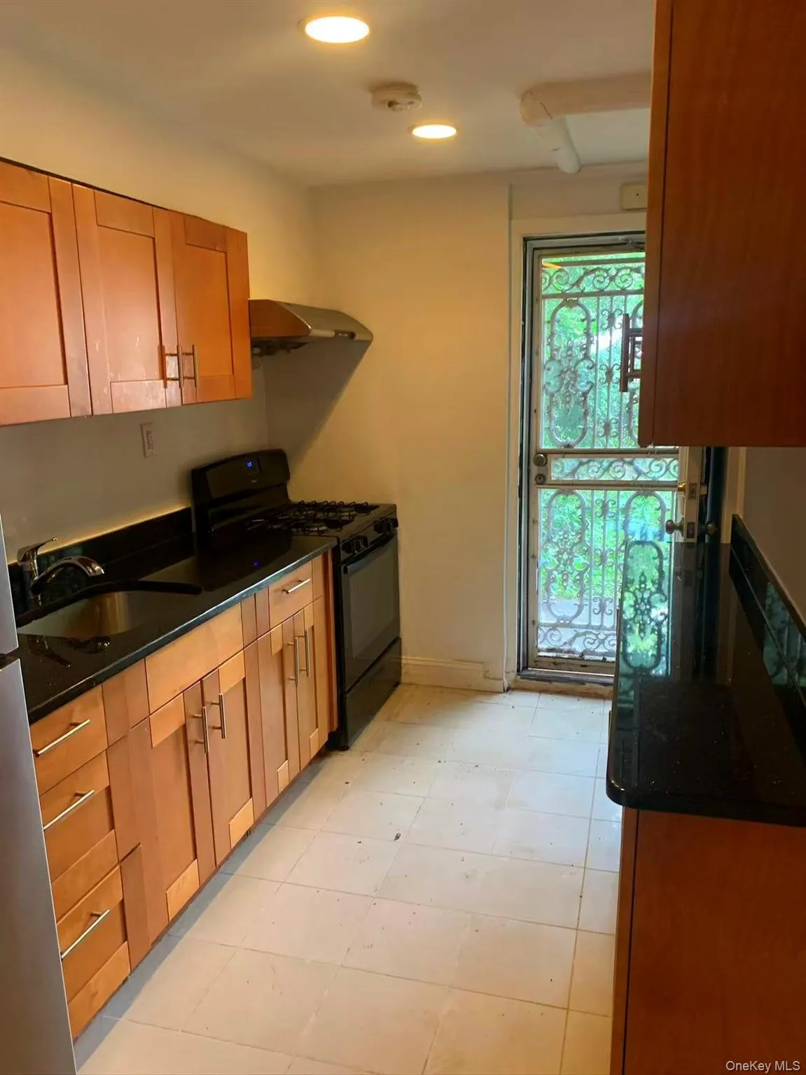 Kitchen with black range with gas cooktop, brown cabinets, recessed lighting, dark stone countertops, and under cabinet range hood Kitchen with black range with gas cooktop, brown cabinets, recessed lighting, dark stone countertops, and under cabinet range hood