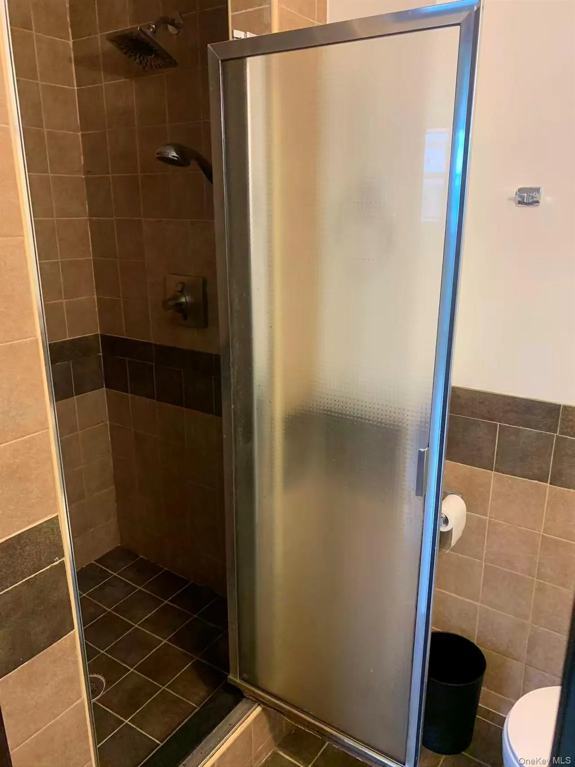 Bathroom with a shower stall, tile walls, and dark tile patterned floors Bathroom with a shower stall, tile walls, and dark tile patterned floors