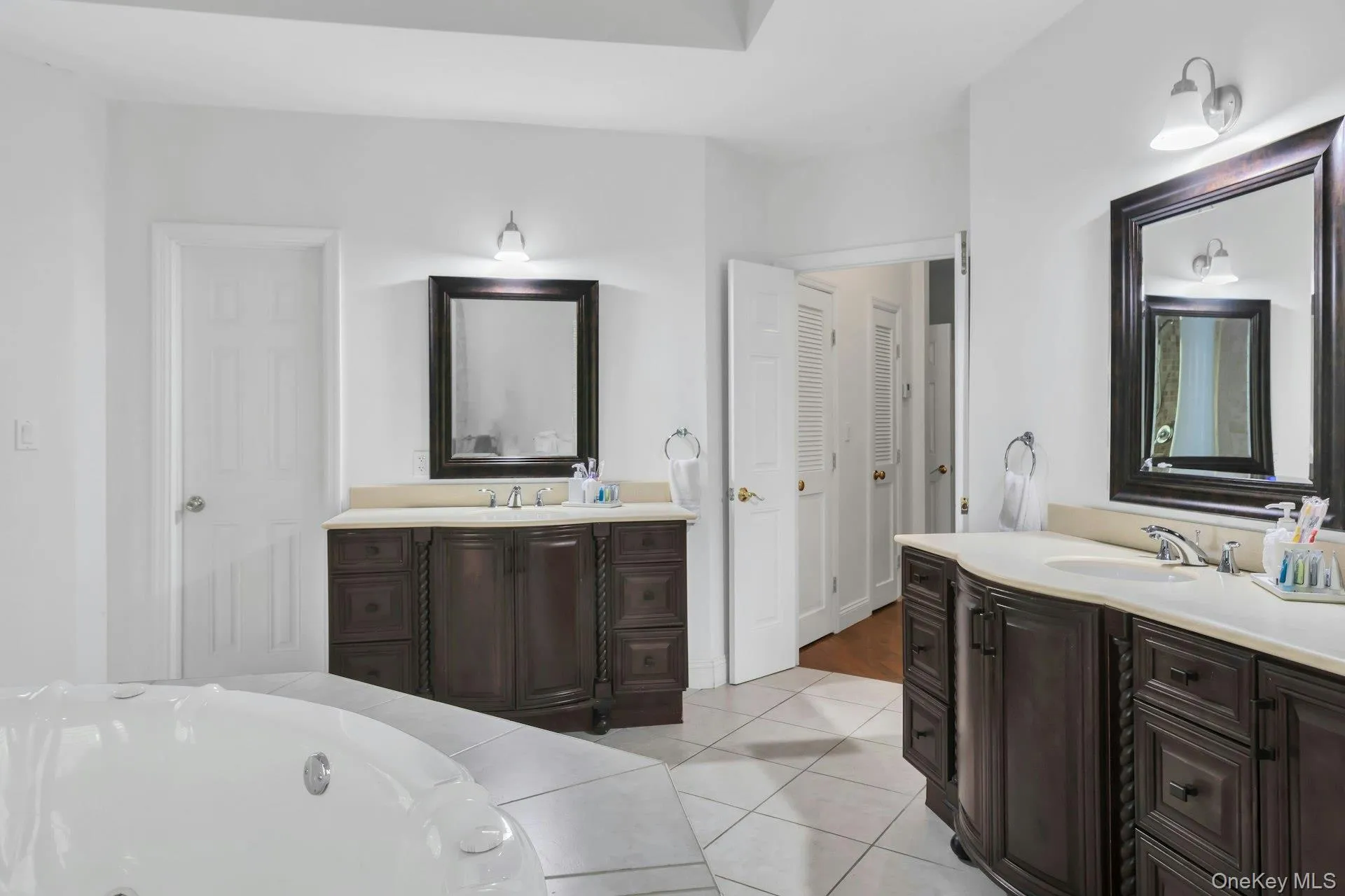 Full bath with two vanities, light tile patterned floors, and a bathtub