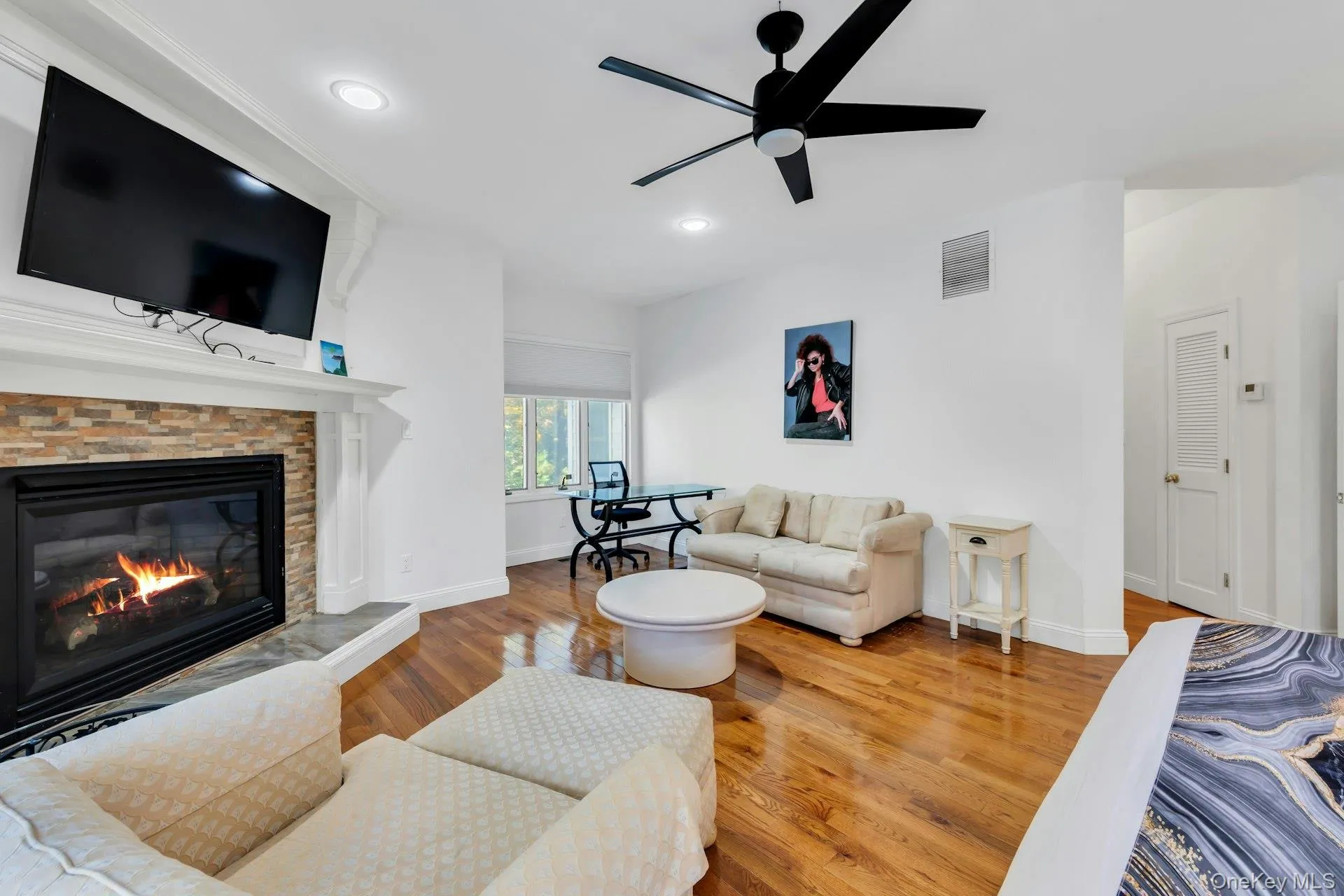 Living room with light wood finished floors, ceiling fan, recessed lighting, and a stone fireplace