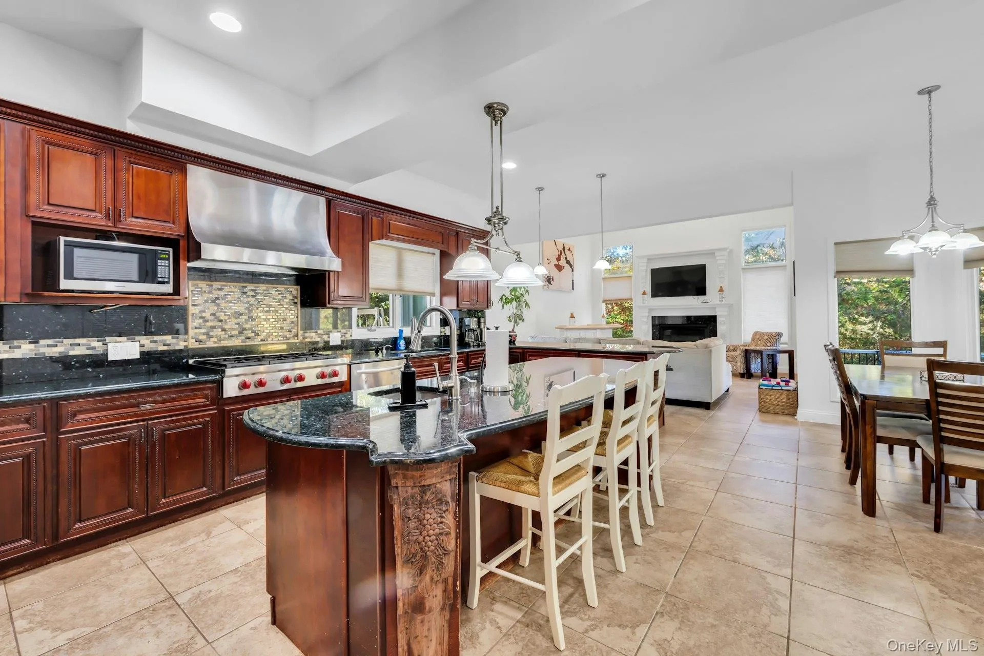 Kitchen featuring dark stone counters, a breakfast bar area, pendant lighting, range hood, and recessed lighting