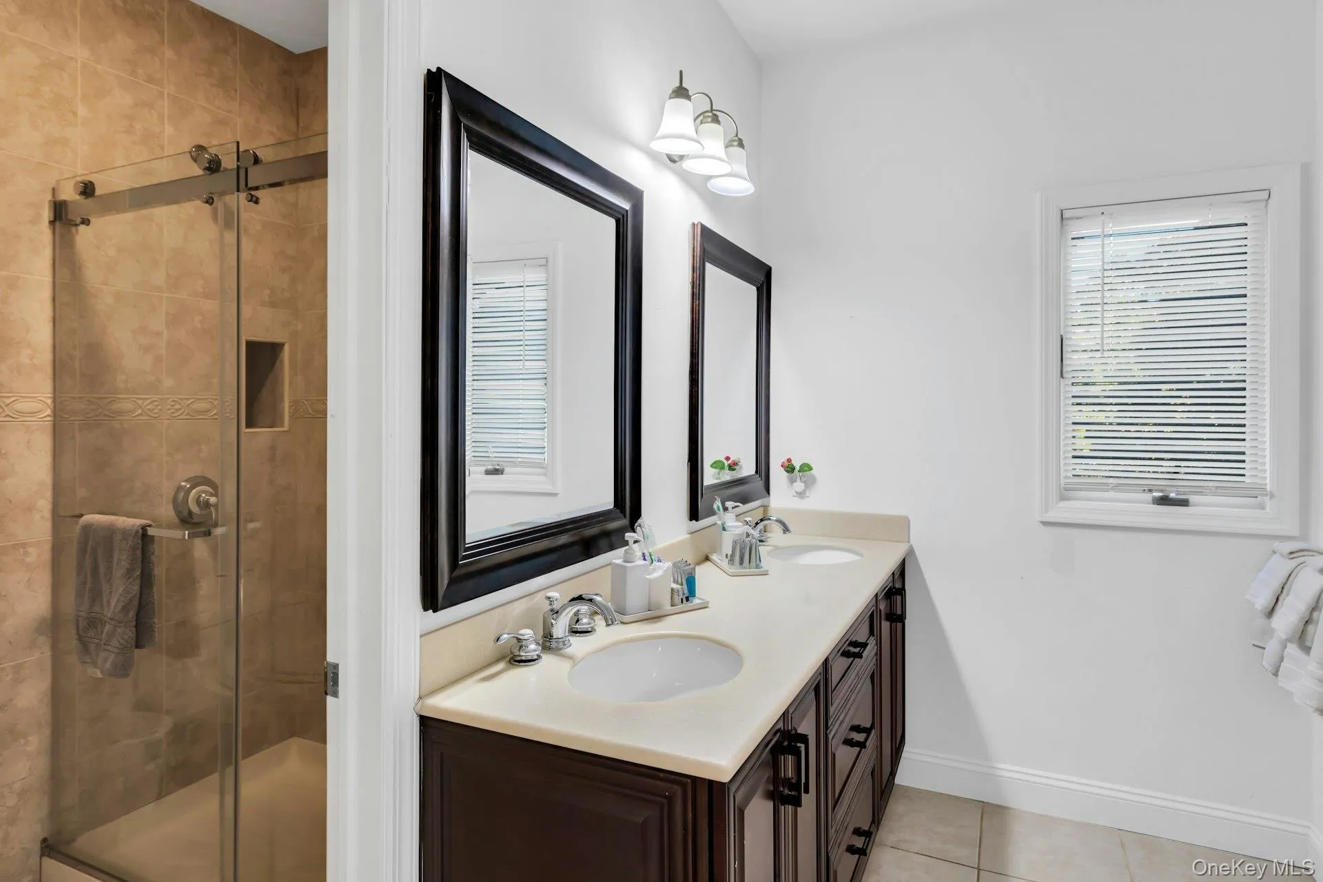 Full bathroom with double vanity, a shower stall, light tile patterned flooring, and healthy amount of natural light