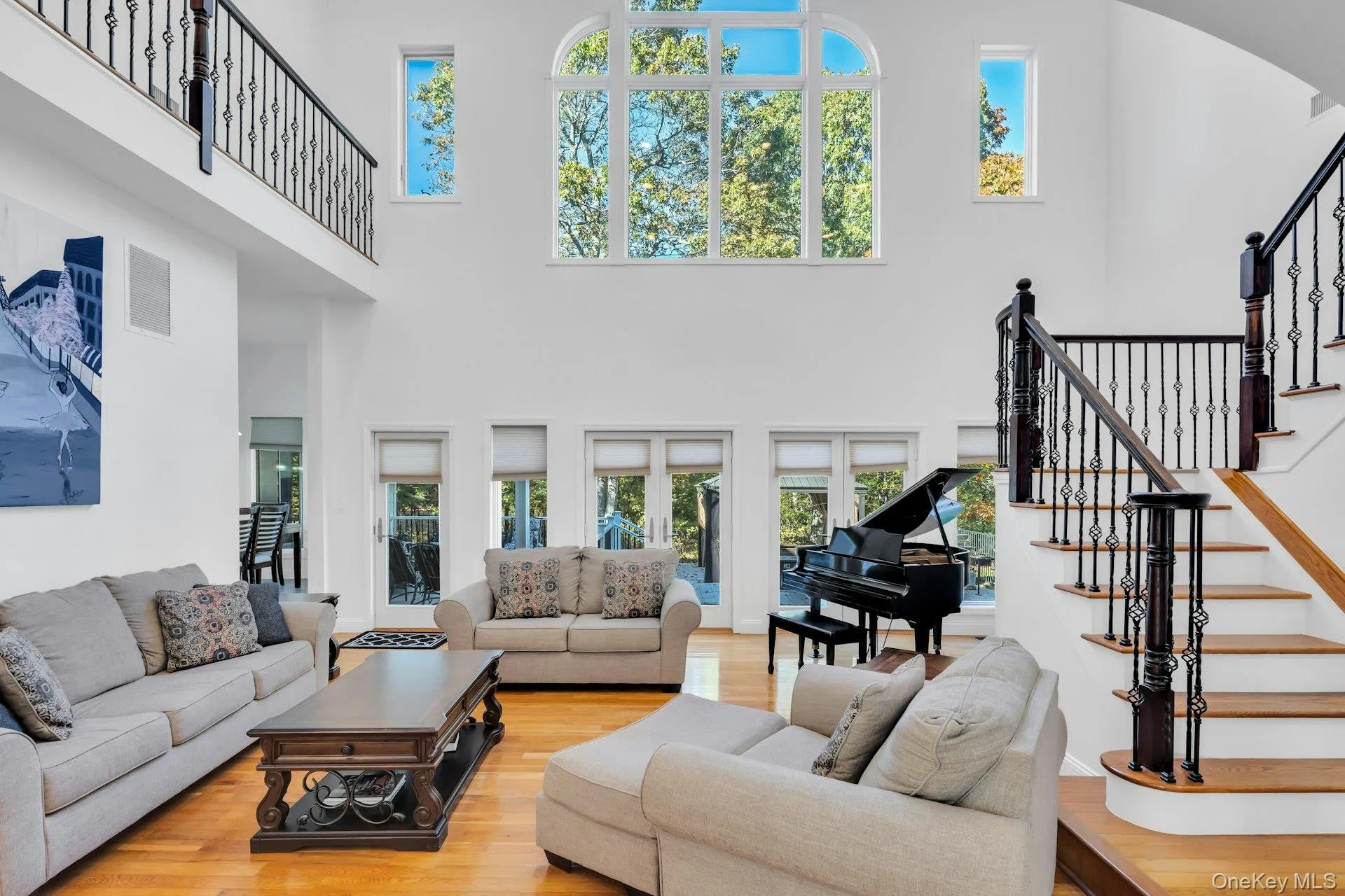 Living room with stairs, light wood finished floors, and a high ceiling