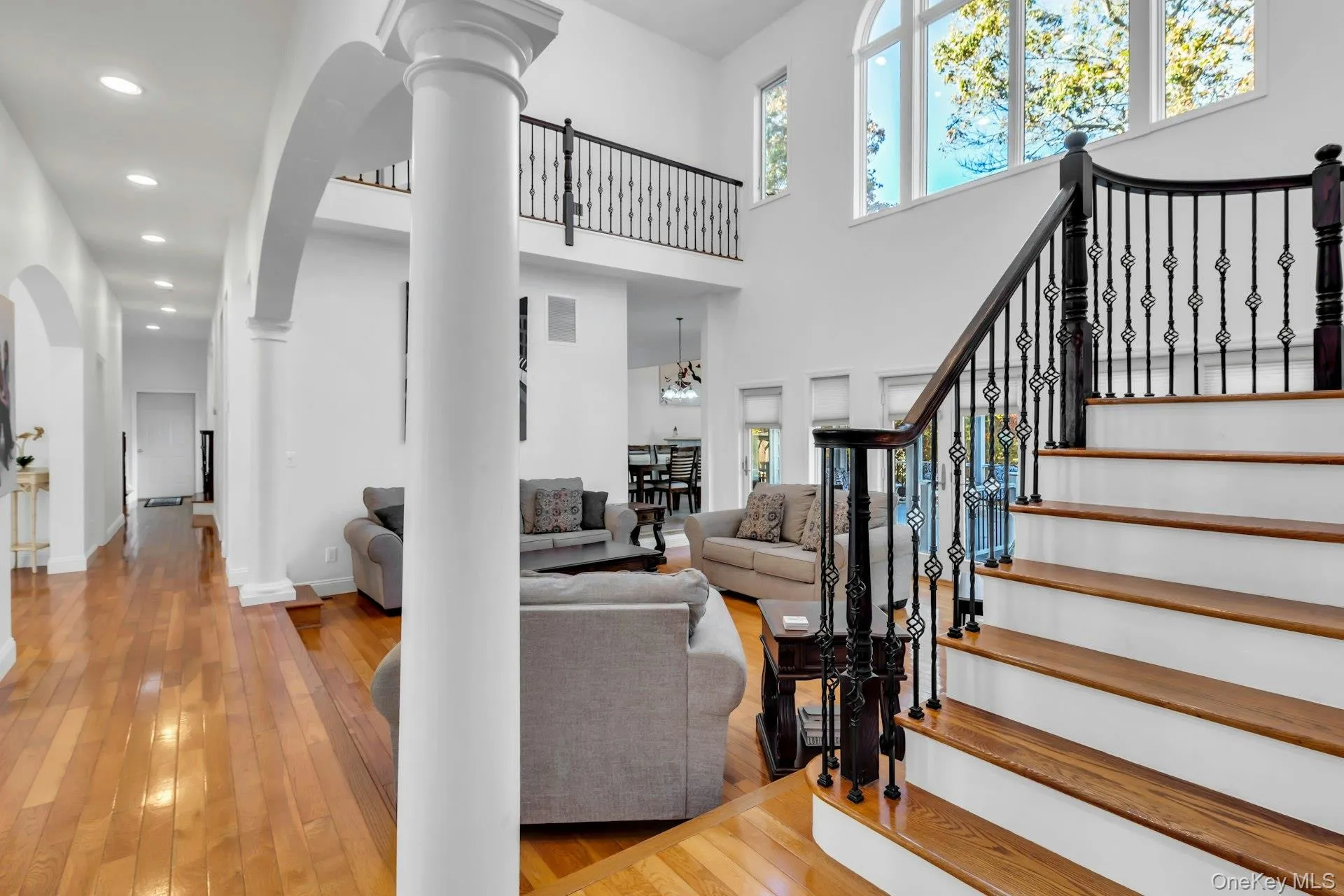 Living area with light wood-style floors, stairway, a high ceiling, recessed lighting, and decorative columns