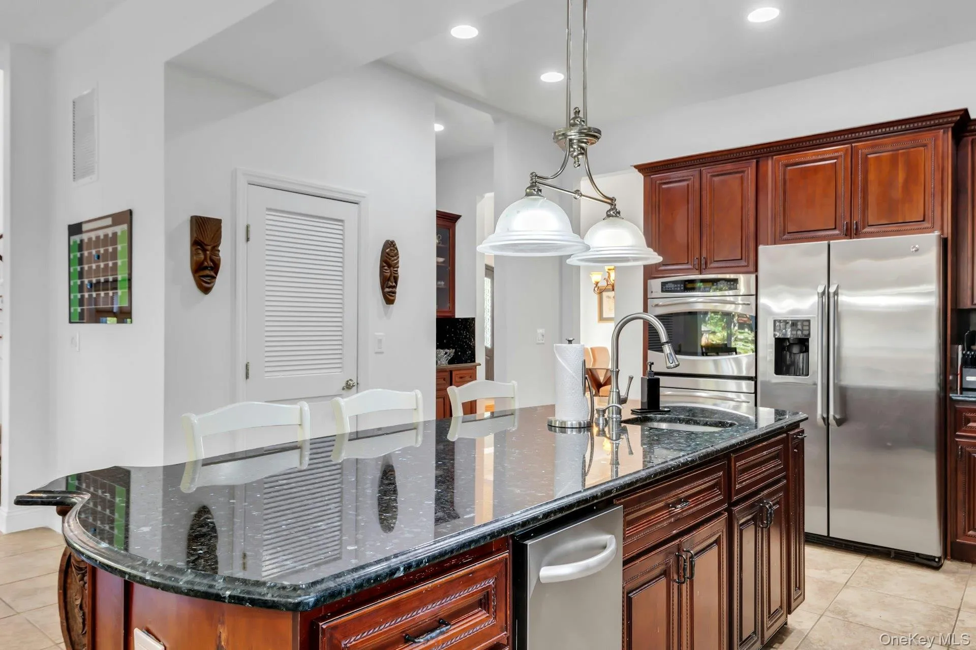 Kitchen with dark stone counters, light tile patterned flooring, stainless steel fridge with ice dispenser, an island with sink, and hanging light fixtures