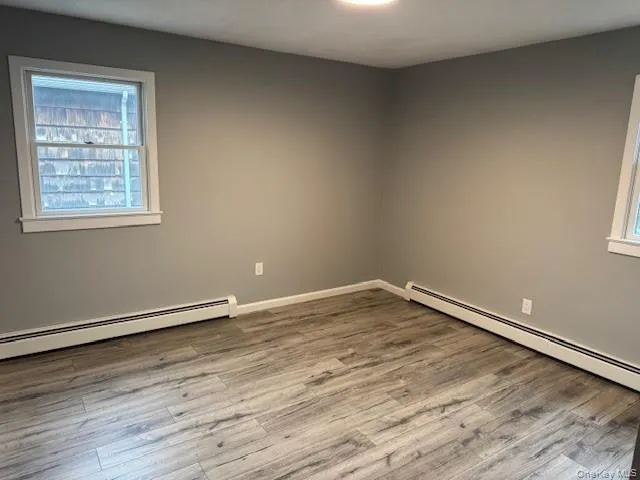 Unfurnished room with wood finished floors and a baseboard heating unit Unfurnished room with wood finished floors and a baseboard heating unit