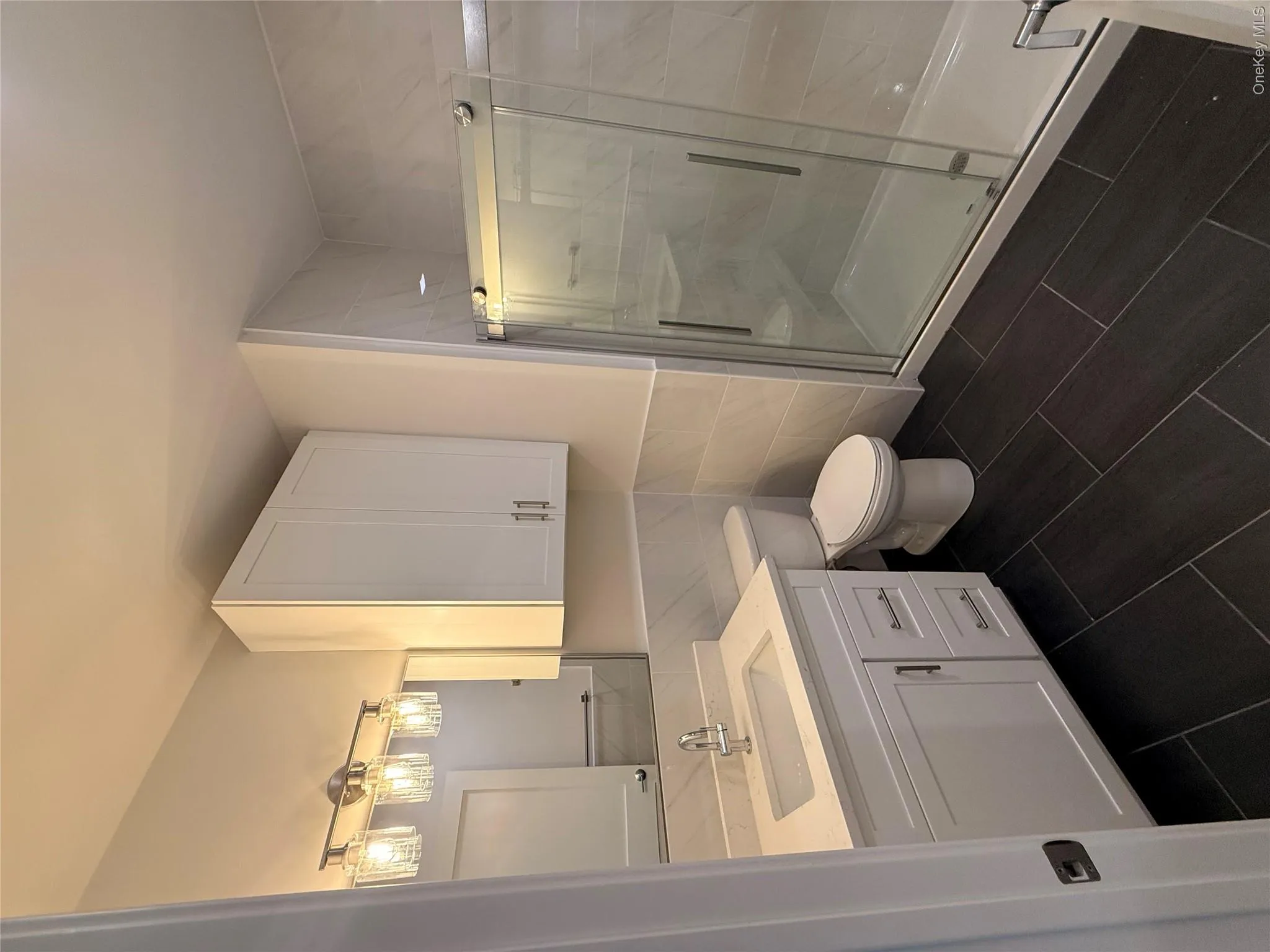 Full bath featuring vanity, a shower stall, tile walls, a wainscoted wall, and dark tile patterned flooring Full bath featuring vanity, a shower stall, tile walls, a wainscoted wall, and dark tile patterned flooring