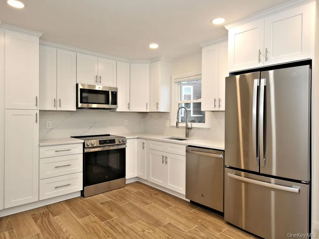 Kitchen with stainless steel appliances, white cabinetry, recessed lighting, wood tiled floors, and decorative backsplash Kitchen with stainless steel appliances, white cabinetry, recessed lighting, wood tiled floors, and decorative backsplash