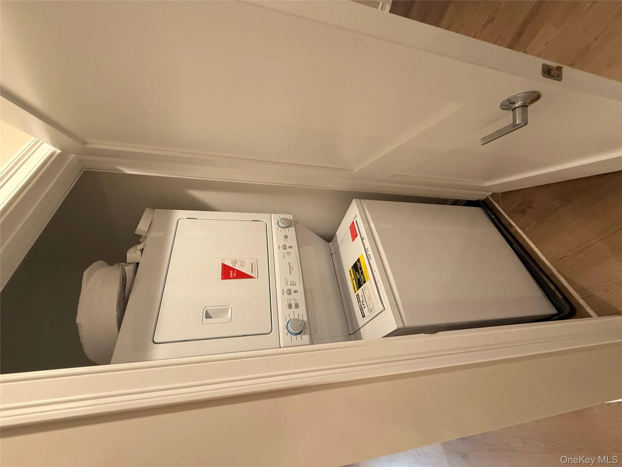 Washroom featuring wood finished floors and stacked washer / drying machine Washroom featuring wood finished floors and stacked washer / drying machine